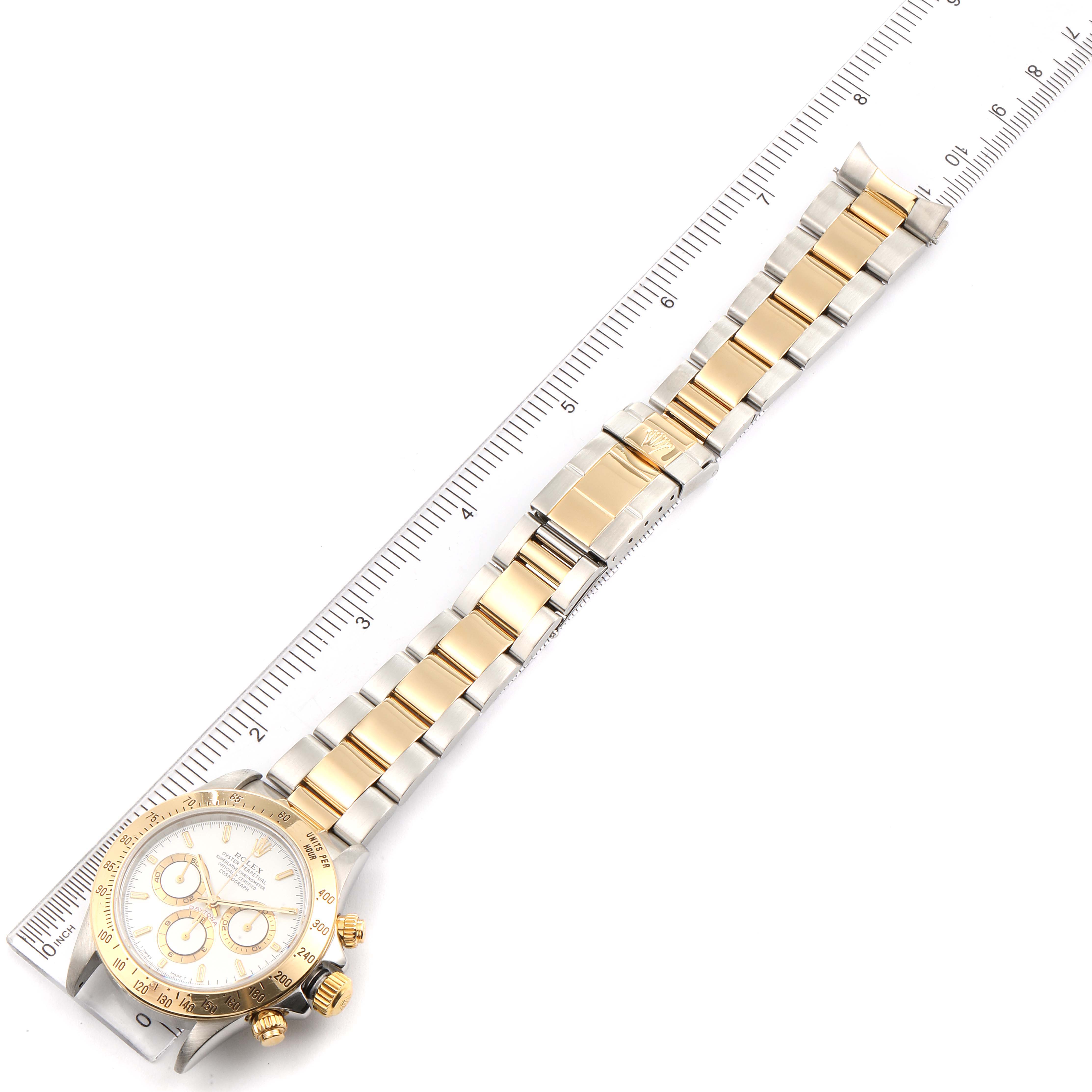 The image shows a Rolex Daytona 16523 Men's Steel and Gold (two tone) White Dial 16523 Men's Steel and Gold (two tone) White Dial watch laid flat, displaying its face, bezel, and bracelet next to a ruler for scale.