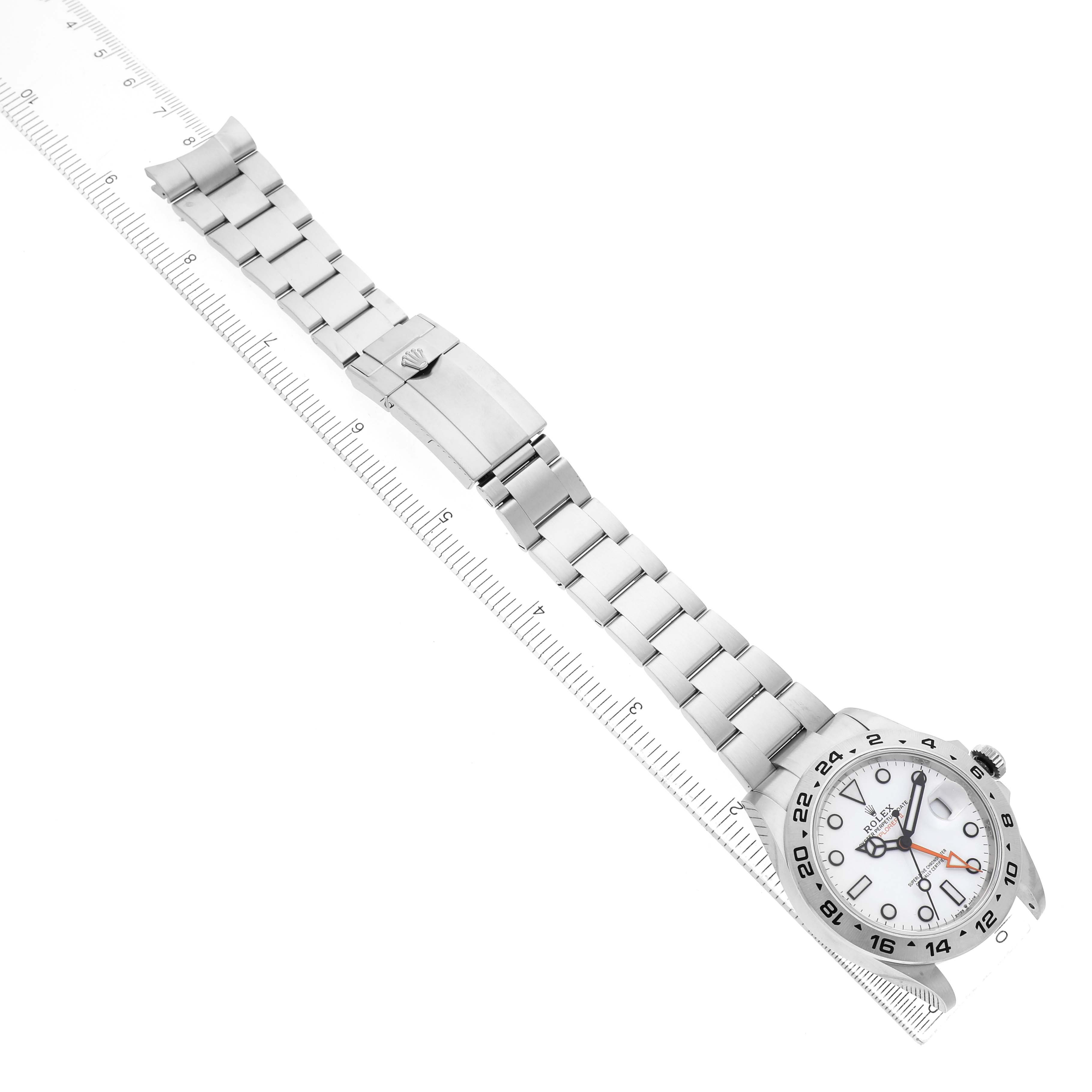 The Rolex Explorer 226570 Men's Stainless Steel White Dial watch is shown from a top-down angle, featuring its face, bezel, bracelet, and clasp aligned next to a ruler.