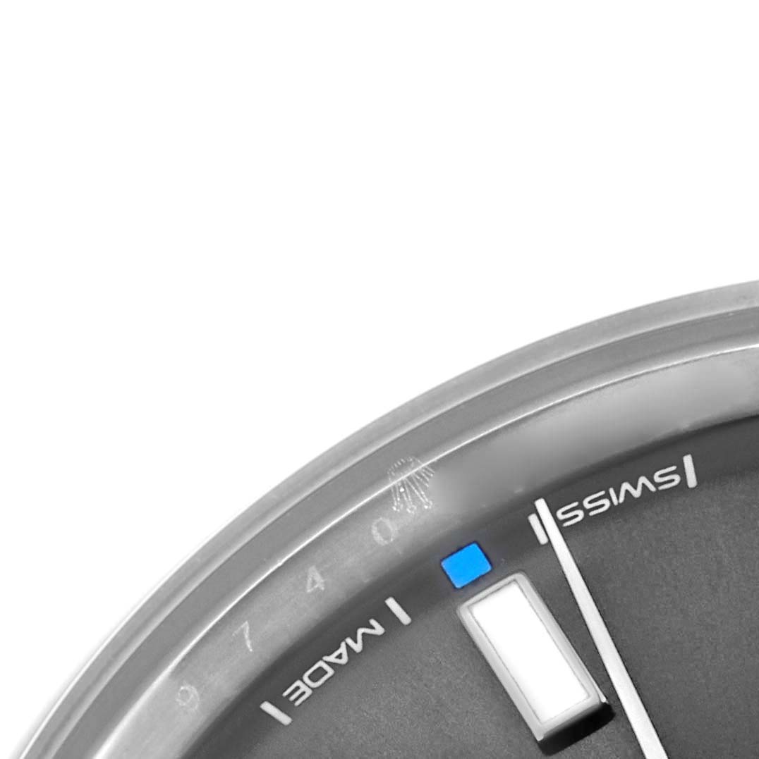 The image shows a close-up of the Rolex Oyster Perpetual 114300 Men's Stainless Steel Grey Dial 114300 Men's Stainless Steel Grey Dial's dial, featuring hour markers, part of the bezel, and "Swiss Made" text.