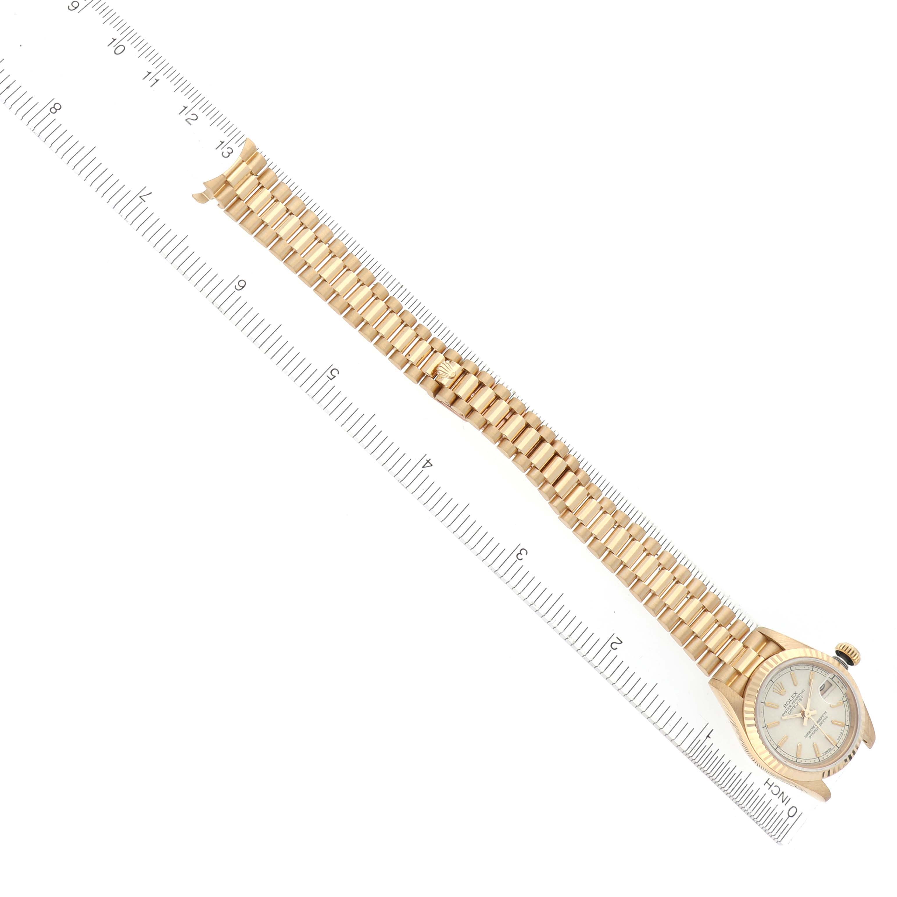 The Rolex President 69178 Women's Yellow Gold White Dial 69178 Women's Yellow Gold White Dial model watch is shown from above, highlighting the bracelet and partially the watch face, with a ruler for scale.