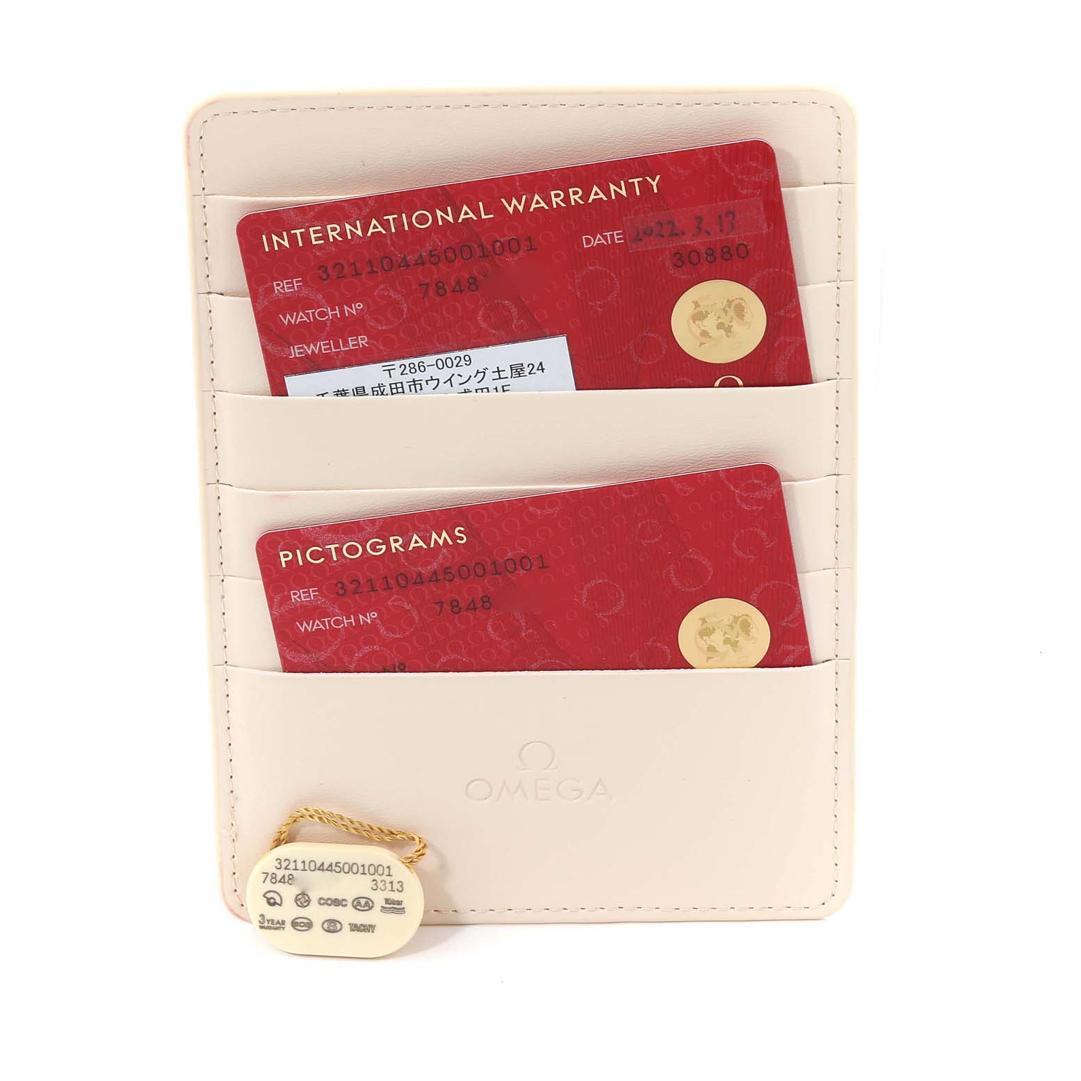 The image shows an Omega Speedmaster 321.10.44.50.01.001 Men
s Stainless Steel Black Dial 321.10.44.50.01.001 Men
s Stainless Steel Black Dial warranty card, pictogram card, and a tag in a beige holder.