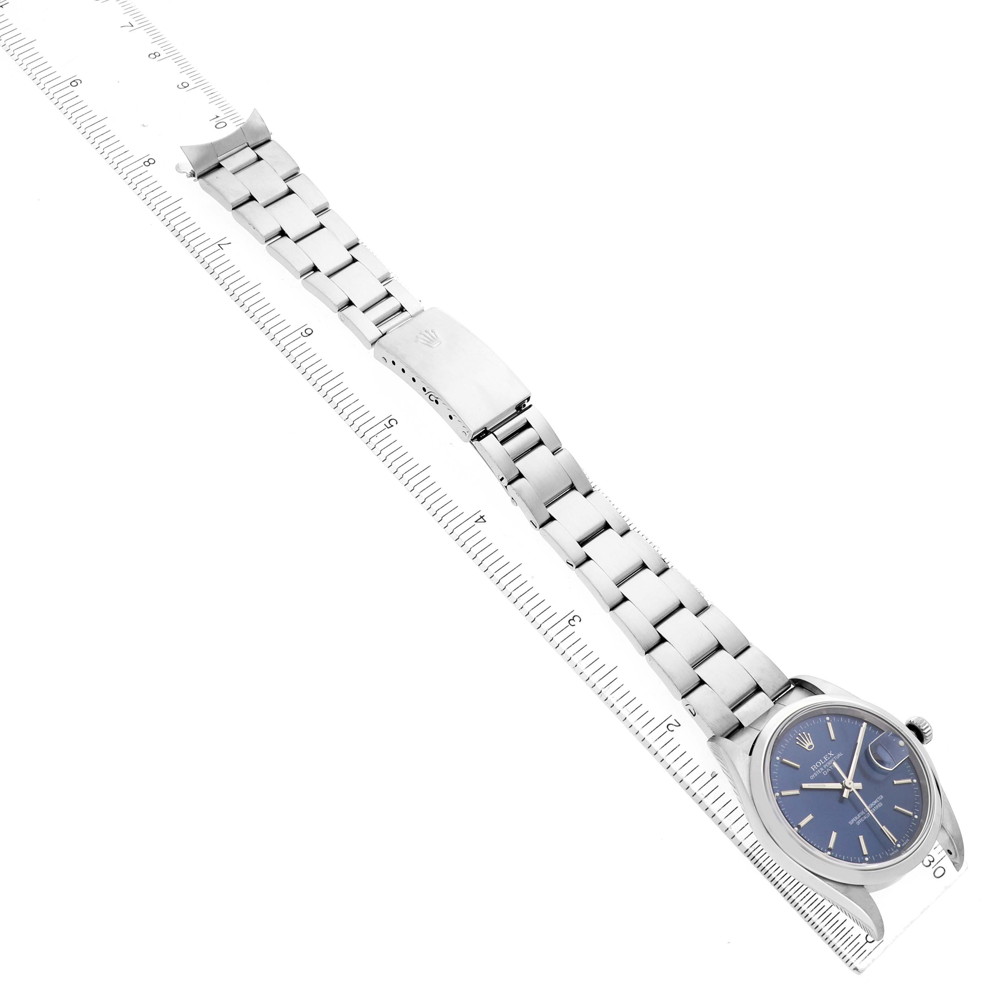 The Rolex Date 15200 Men's Stainless Steel Blue Dial watch is shown at an angle displaying its full bracelet, clasp, and blue dial, with a ruler for size reference.