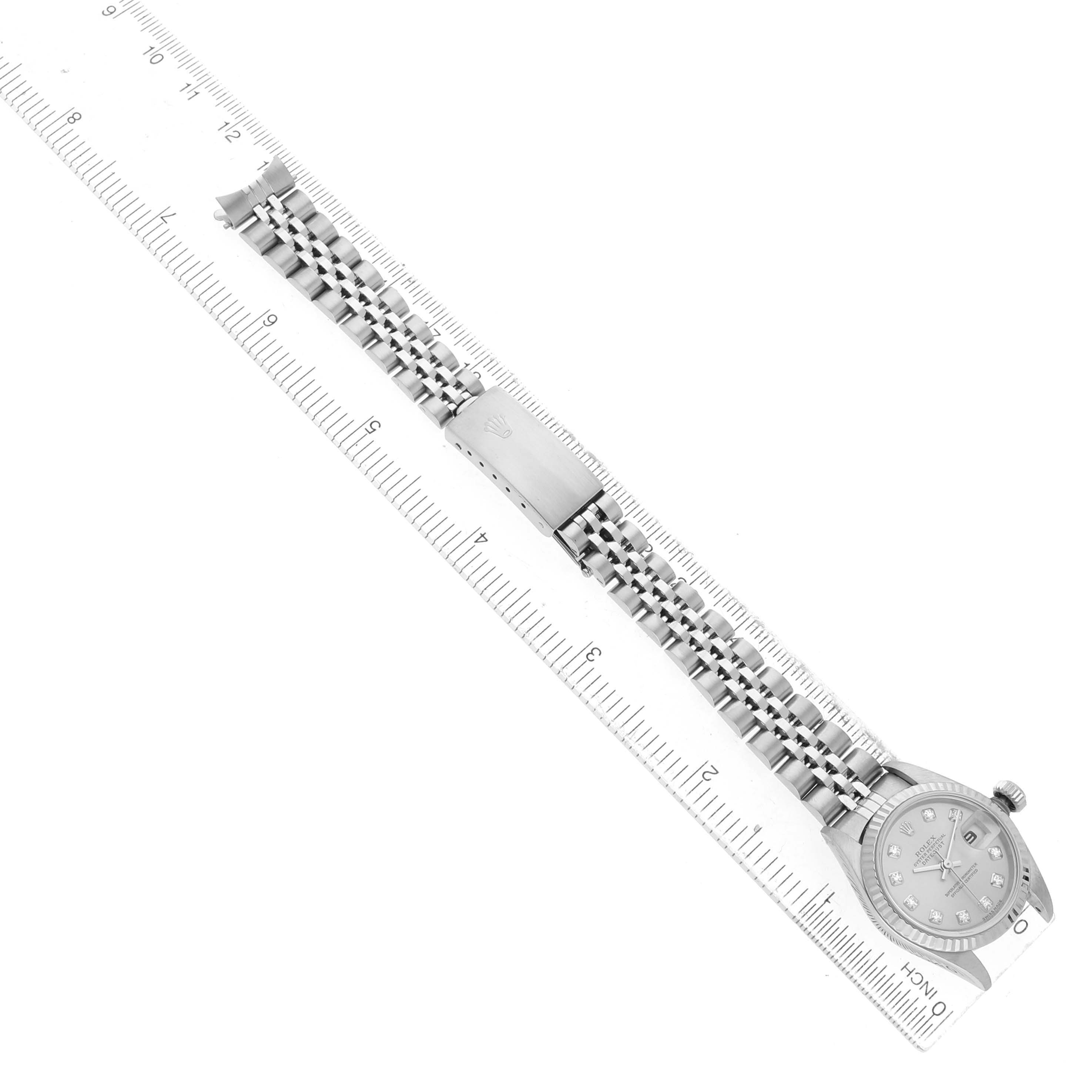 The Rolex Datejust 79174 Women's Stainless Steel Silver Dial watch is shown from a top-down angle, displaying the face, bracelet, and clasp, alongside a ruler for scale.