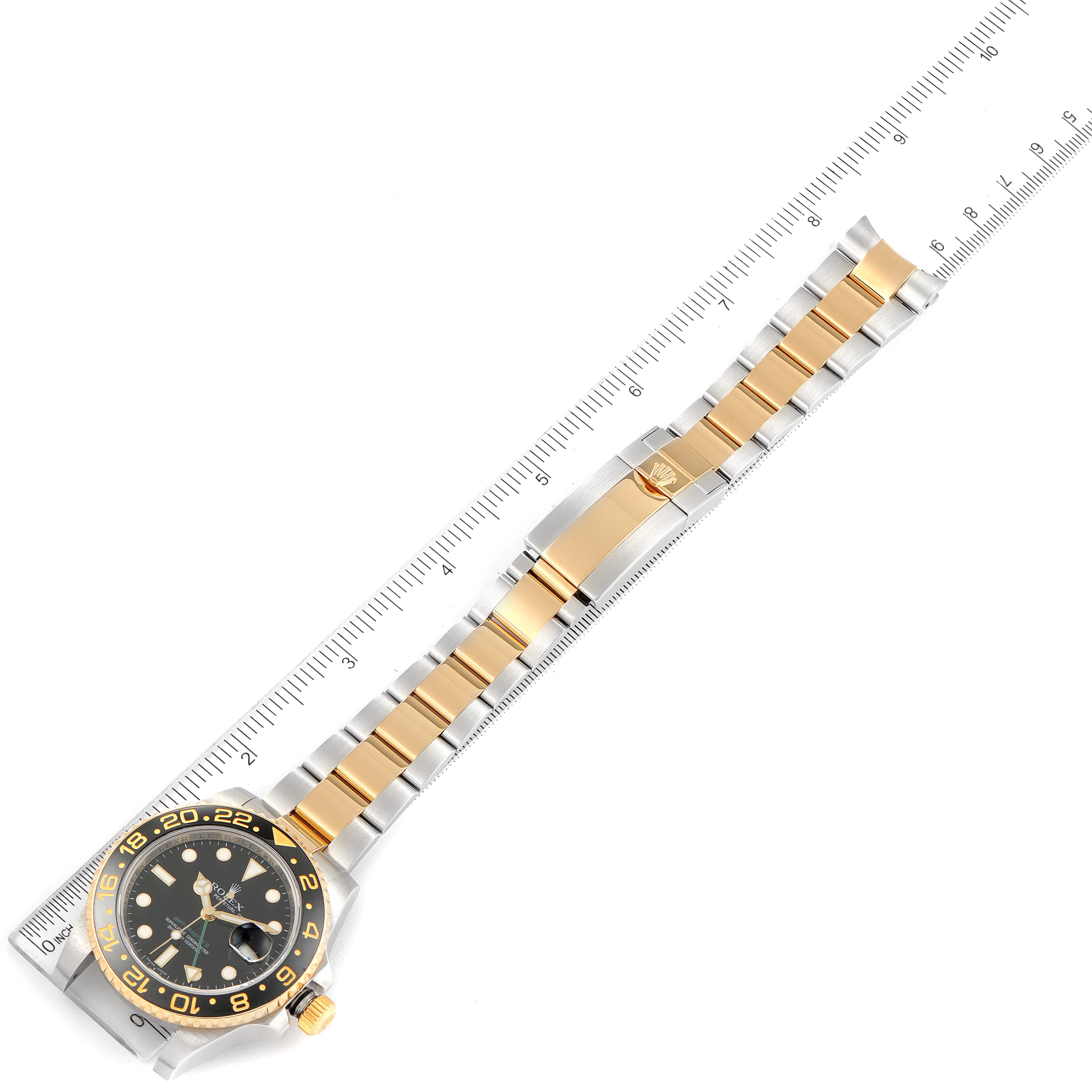 This image shows a Rolex GMT-Master 116713 Men's Steel and Gold (two tone) Black Dial 116713 Men's Steel and Gold (two tone) Black Dial watch laid flat with a ruler, highlighting its bezel, dial, and two-tone bracelet.