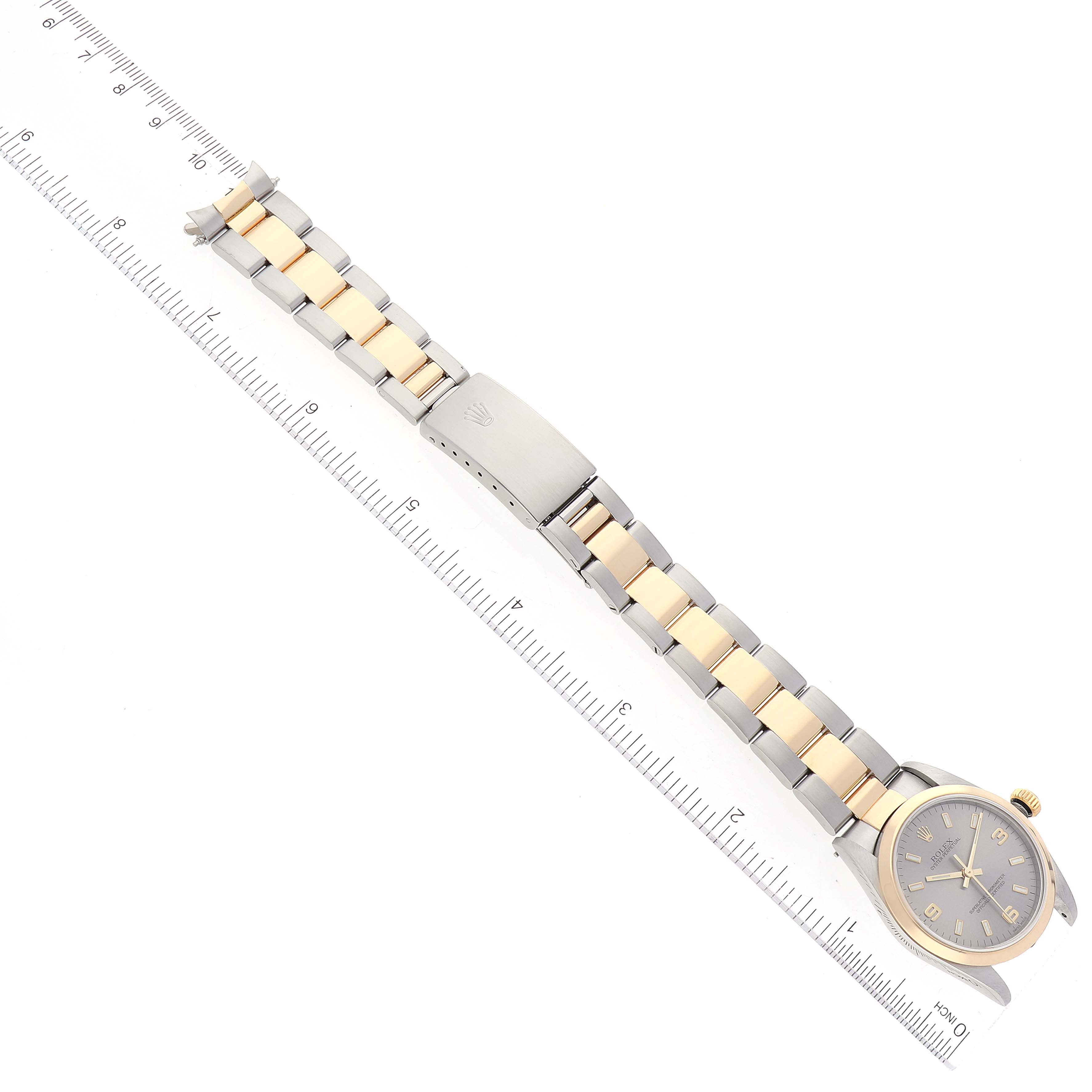 The image shows a top-down view of a Rolex Mid-Size 77483 Women
s Steel and Gold (two tone) Grey Dial 77483 Women
s Steel and Gold (two tone) Grey Dial watch with its full bracelet and clasp, alongside a ruler for scale.