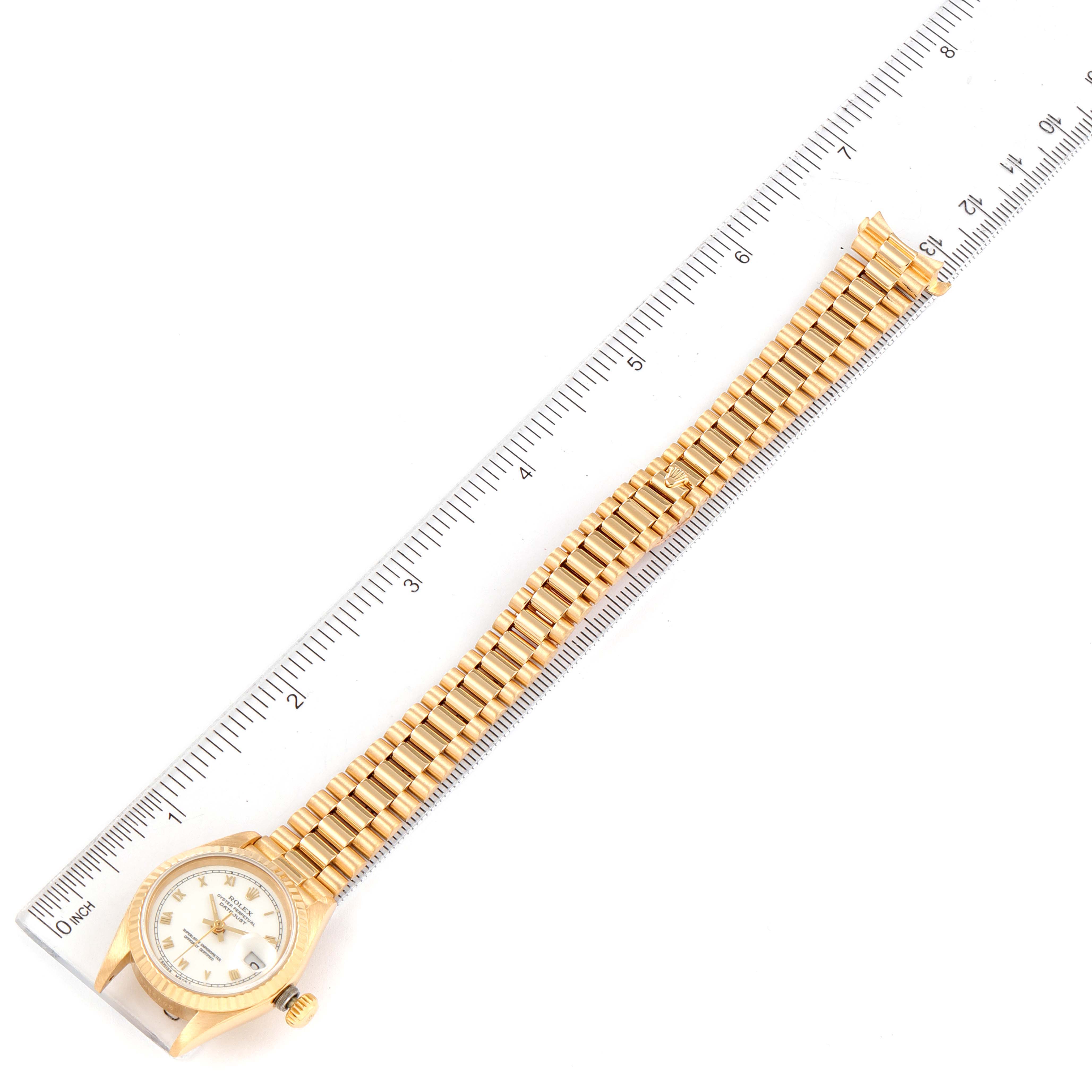 This is a top-down view of a Rolex President 69178 Women
s Yellow Gold White Dial 69178 Women
s Yellow Gold White Dial watch showcasing its face, bezel, and bracelet beside a ruler for scale.