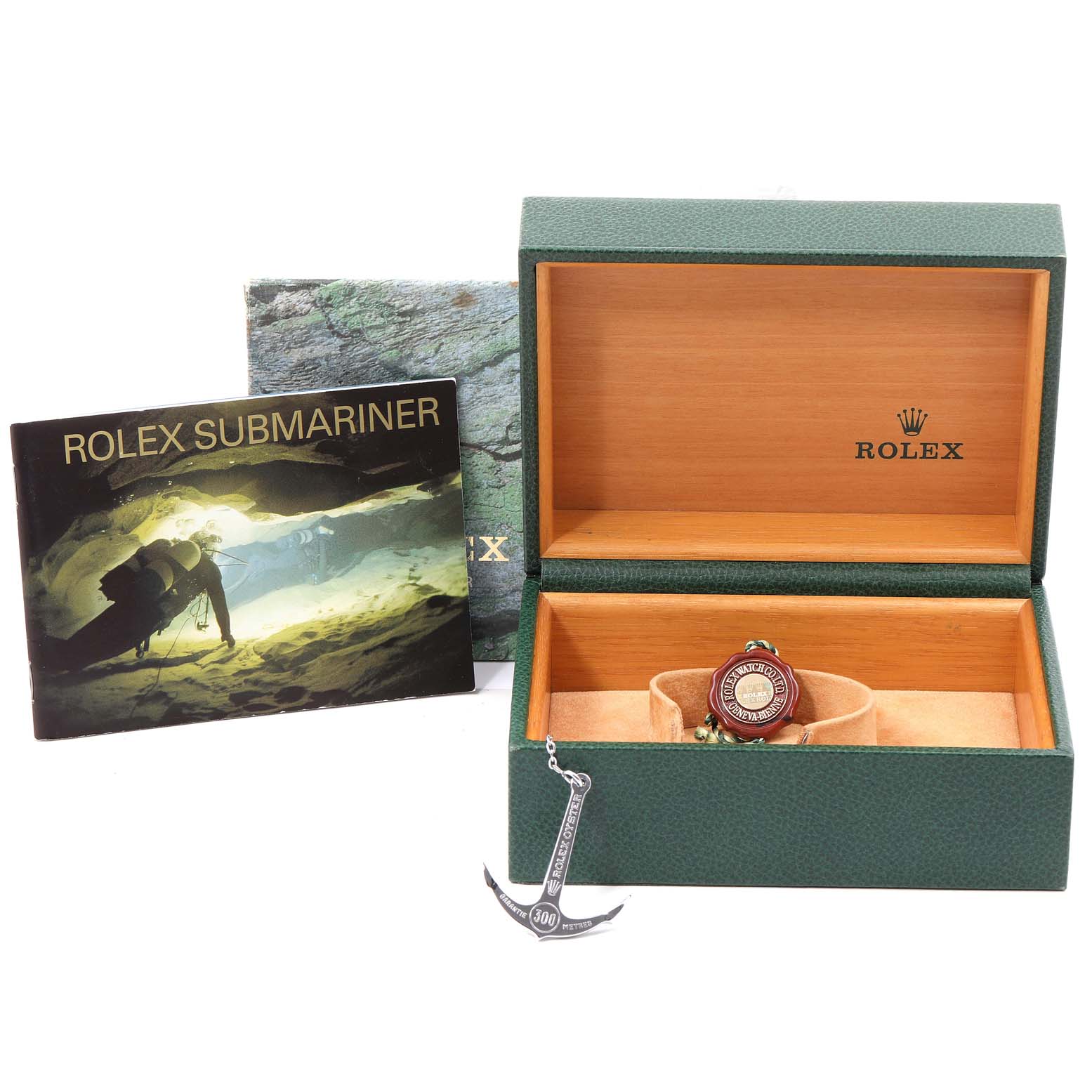 The image shows a Rolex Submariner 16610 Men's Stainless Steel Black Dial 16610 Men's Stainless Steel Black Dial watch box, an anchor-shaped accessory, and a booklet, all taken from a front angle.