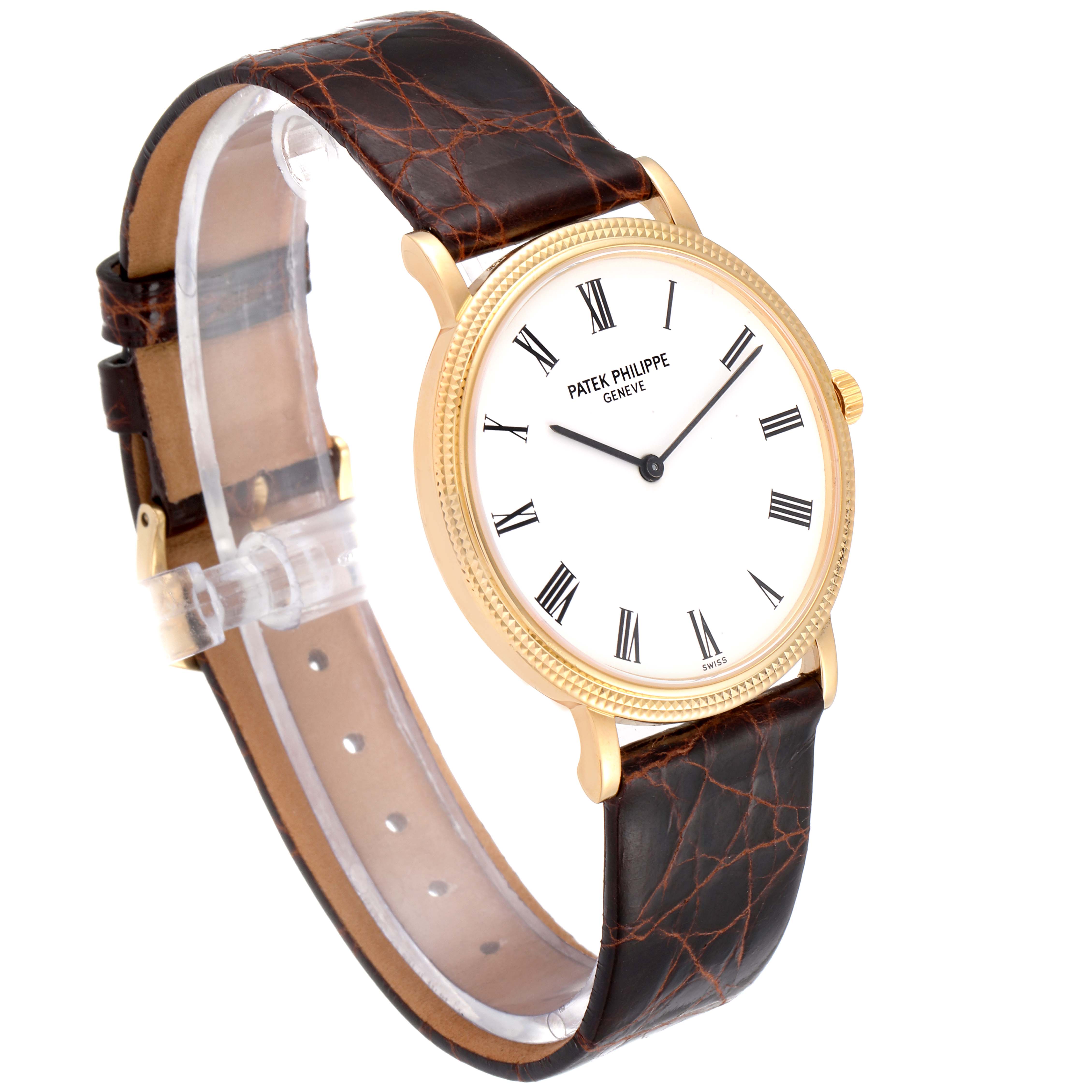 The Patek Philippe Calatrava 5120J Men's Yellow Gold White Dial 5120J Men's Yellow Gold White Dial watch is shown at an angled side view, displaying its gold case, white dial with Roman numerals, and brown leather strap.