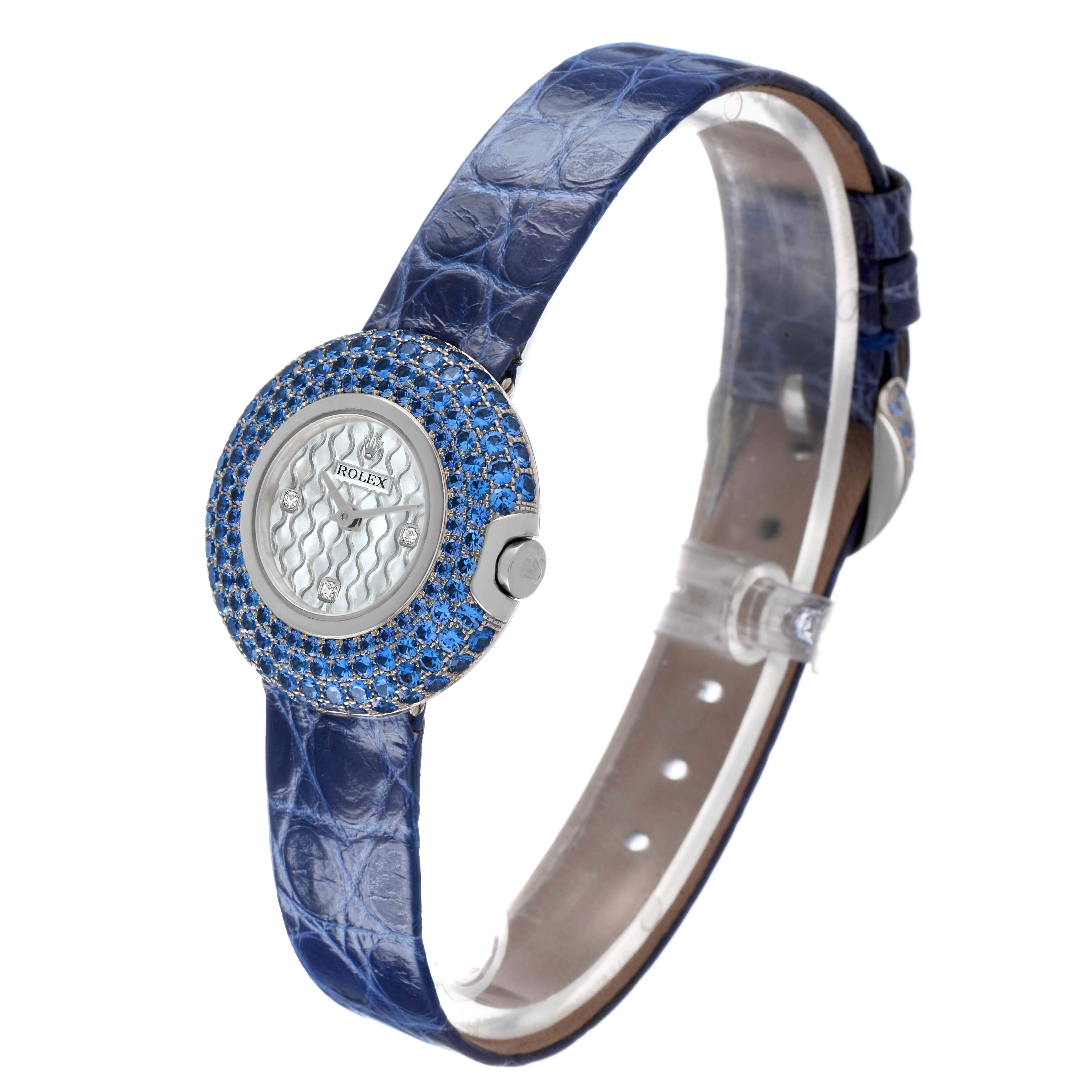 The Rolex Cellini 6201 Women's White Gold Mother of Pearl Dial watch is shown at a diagonal angle, highlighting its blue gemstone bezel and leather strap.