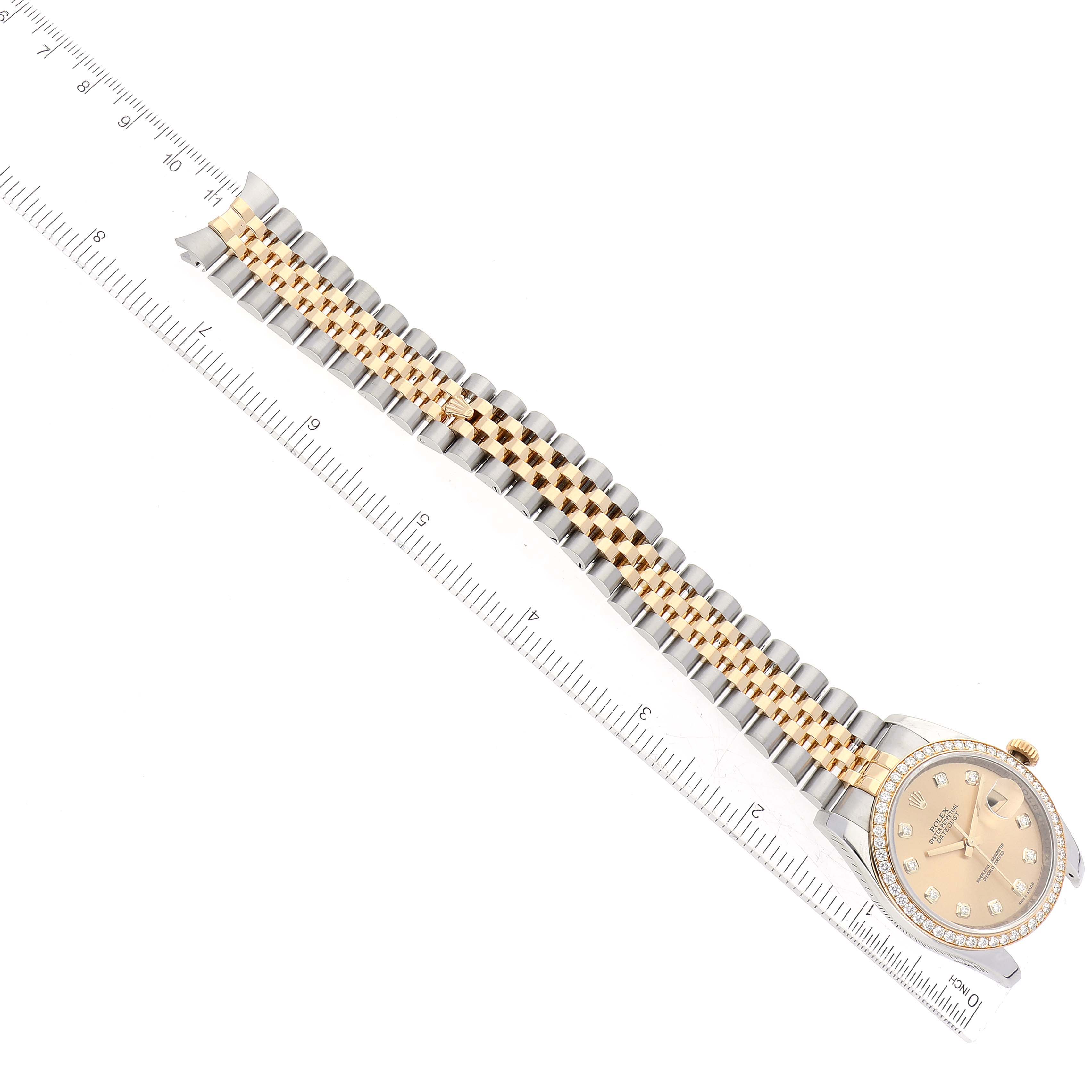 The Rolex Datejust 116243 Men's Steel and Gold (two tone) Champagne Dial 116243 Men's Steel and Gold (two tone) Champagne Dial watch is shown from a top-down angle, highlighting its bracelet and dial next to a ruler for scale.