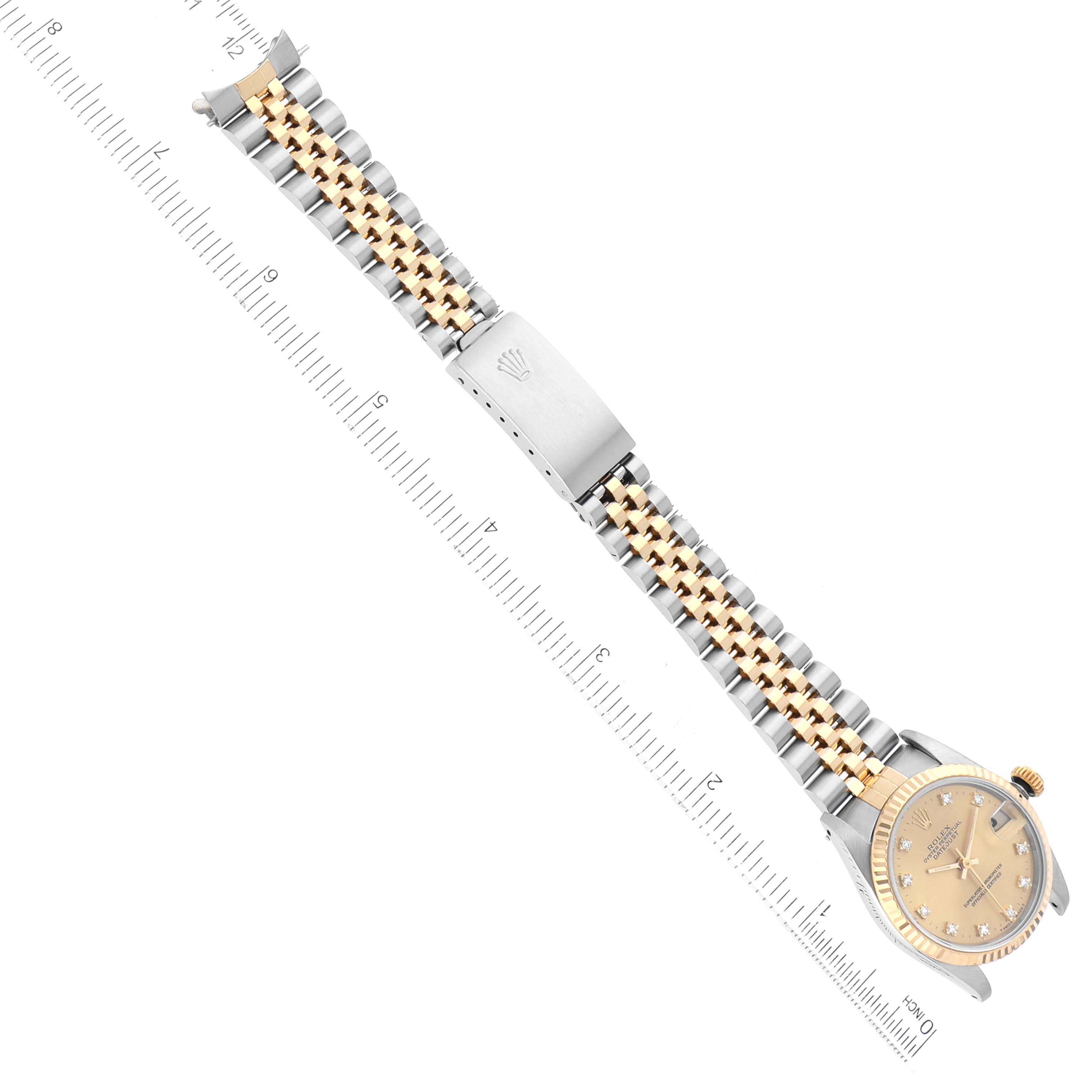 The Rolex Mid-Size 68273G Women's Steel and Gold (two tone) Champagne Dial 68273G Women's Steel and Gold (two tone) Champagne Dial watch is shown from a top-down angle, displaying its dial, case, and two-tone bracelet fully extended next to a ruler.
