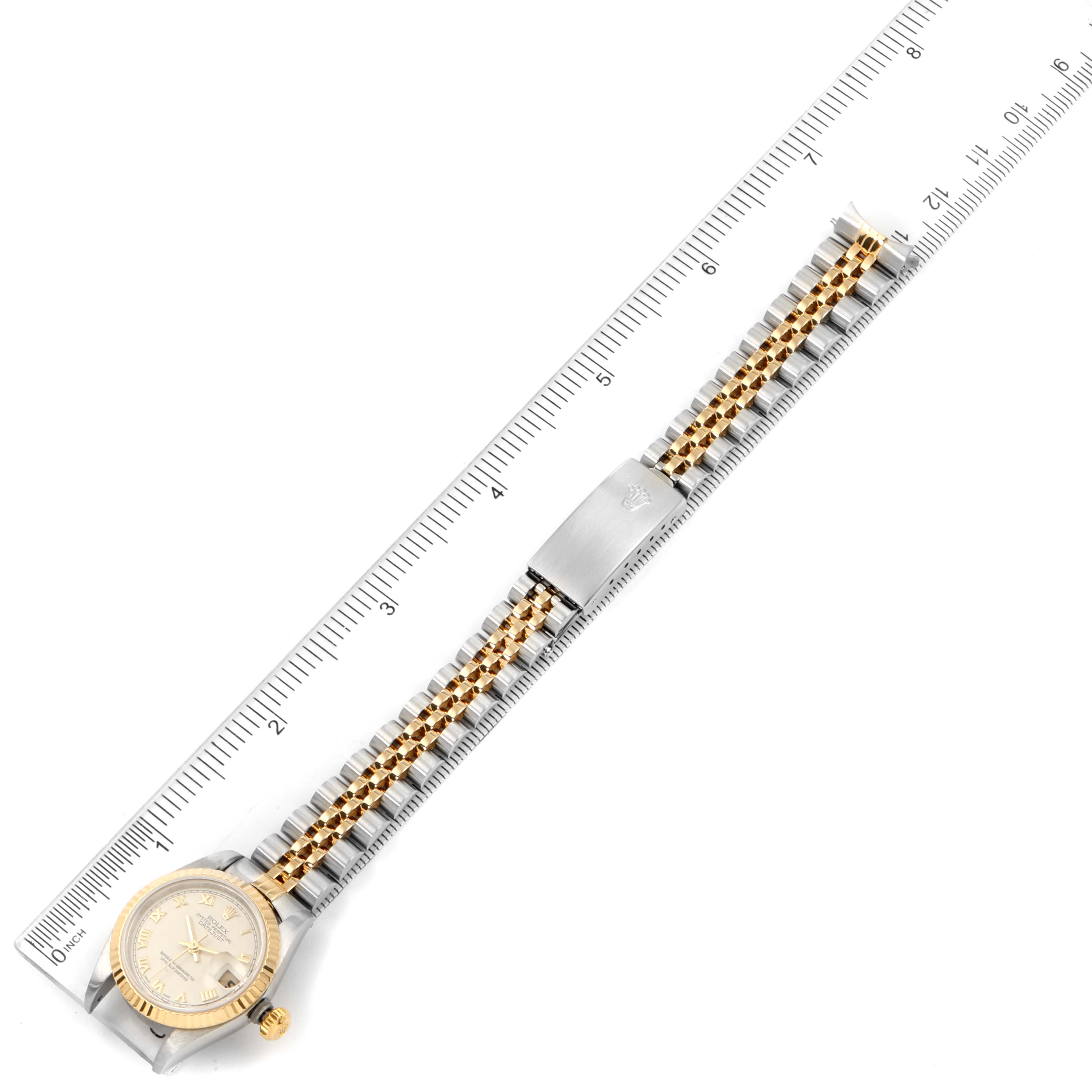 The Rolex Datejust 79173 Women's Steel and Gold (two tone) Beige Dial 79173 Women's Steel and Gold (two tone) Beige Dial watch is shown from a top-down angle with its gold and silver bracelet fully extended alongside a ruler for scale.