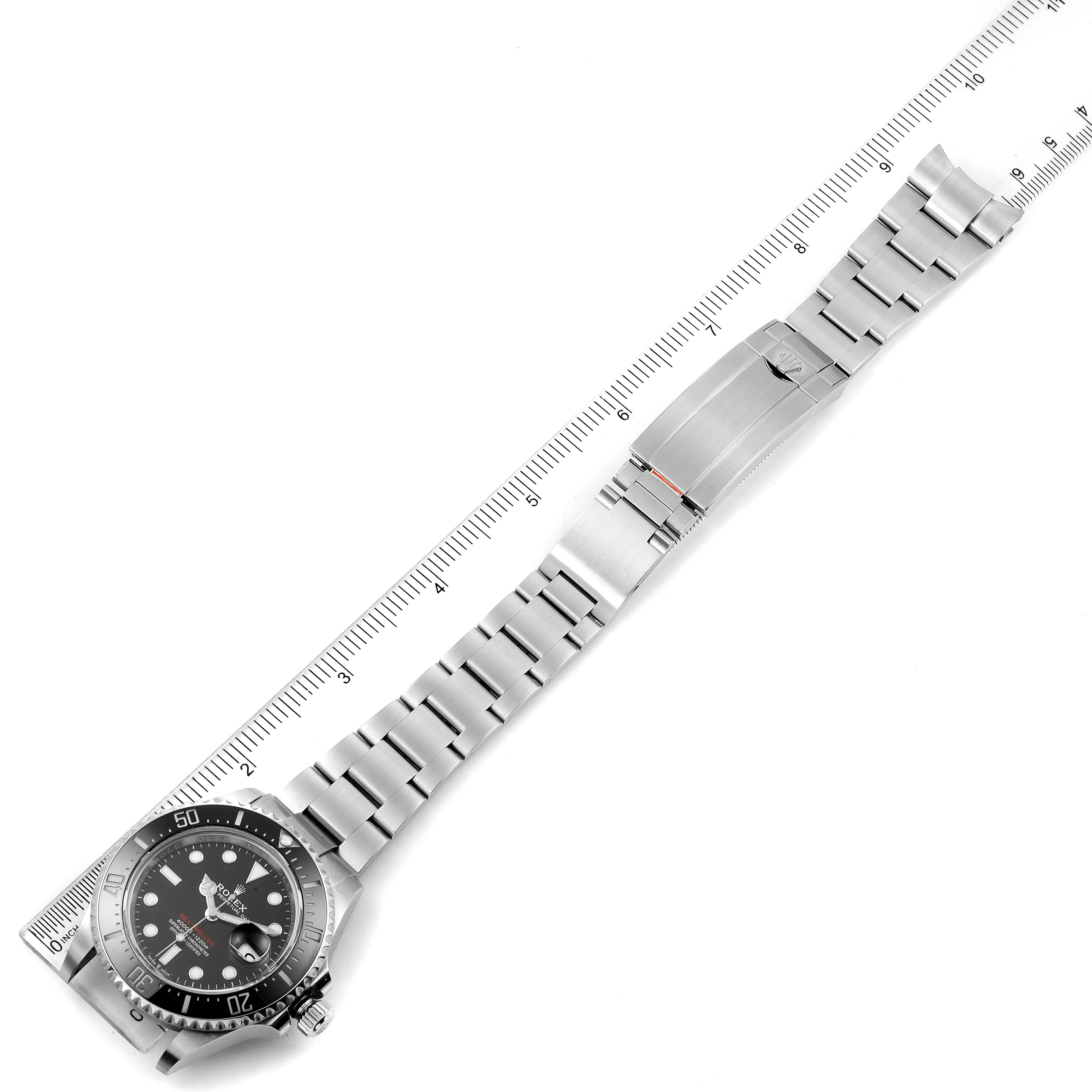 The image shows a top-down view of a Rolex Sea-Dweller 126600 Men
s Stainless Steel Black Dial 126600 Men
s Stainless Steel Black Dial watch laid out beside a ruler, showcasing its face and band.