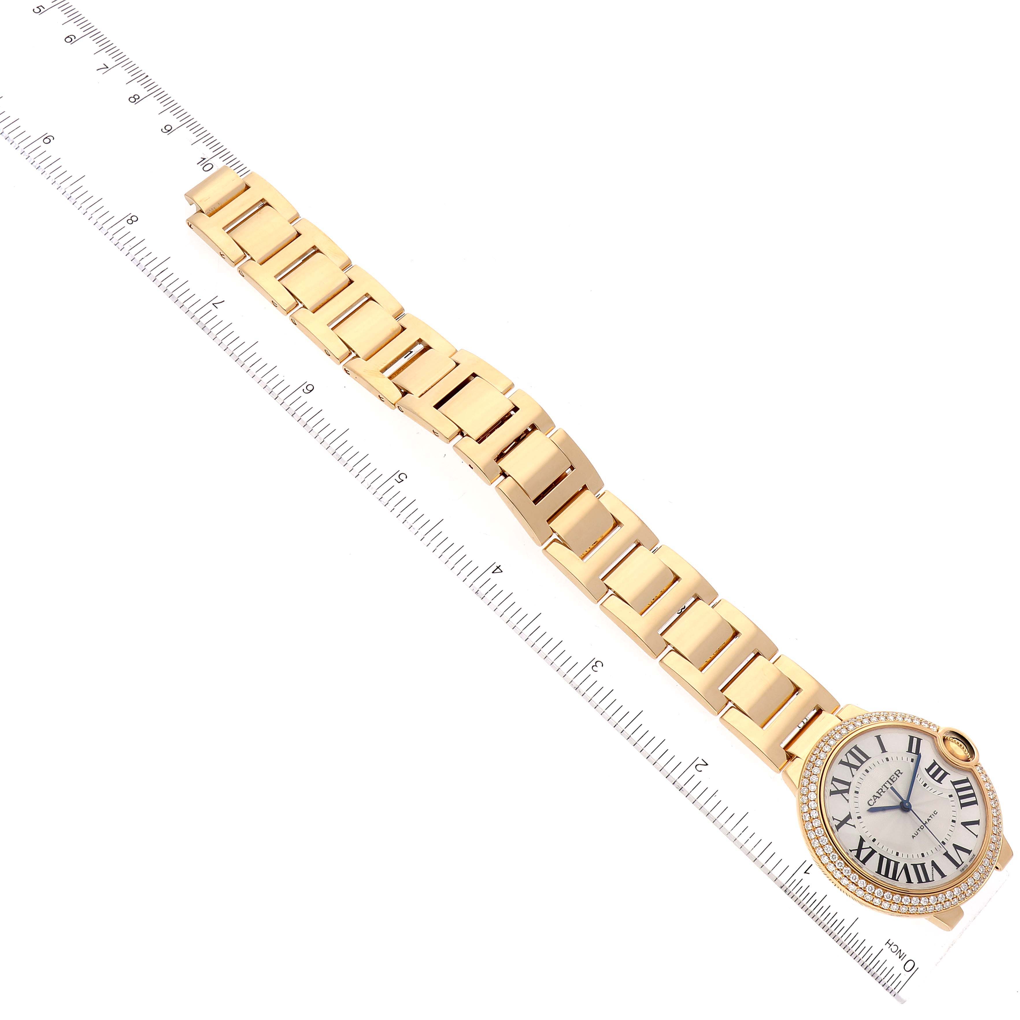The image shows an angled top view of a Cartier Ballon Bleu WE9004Z3 Women
s Yellow Gold Silver Dial WE9004Z3 Women
s Yellow Gold Silver Dial watch with a gold bracelet and a ruler for scale.