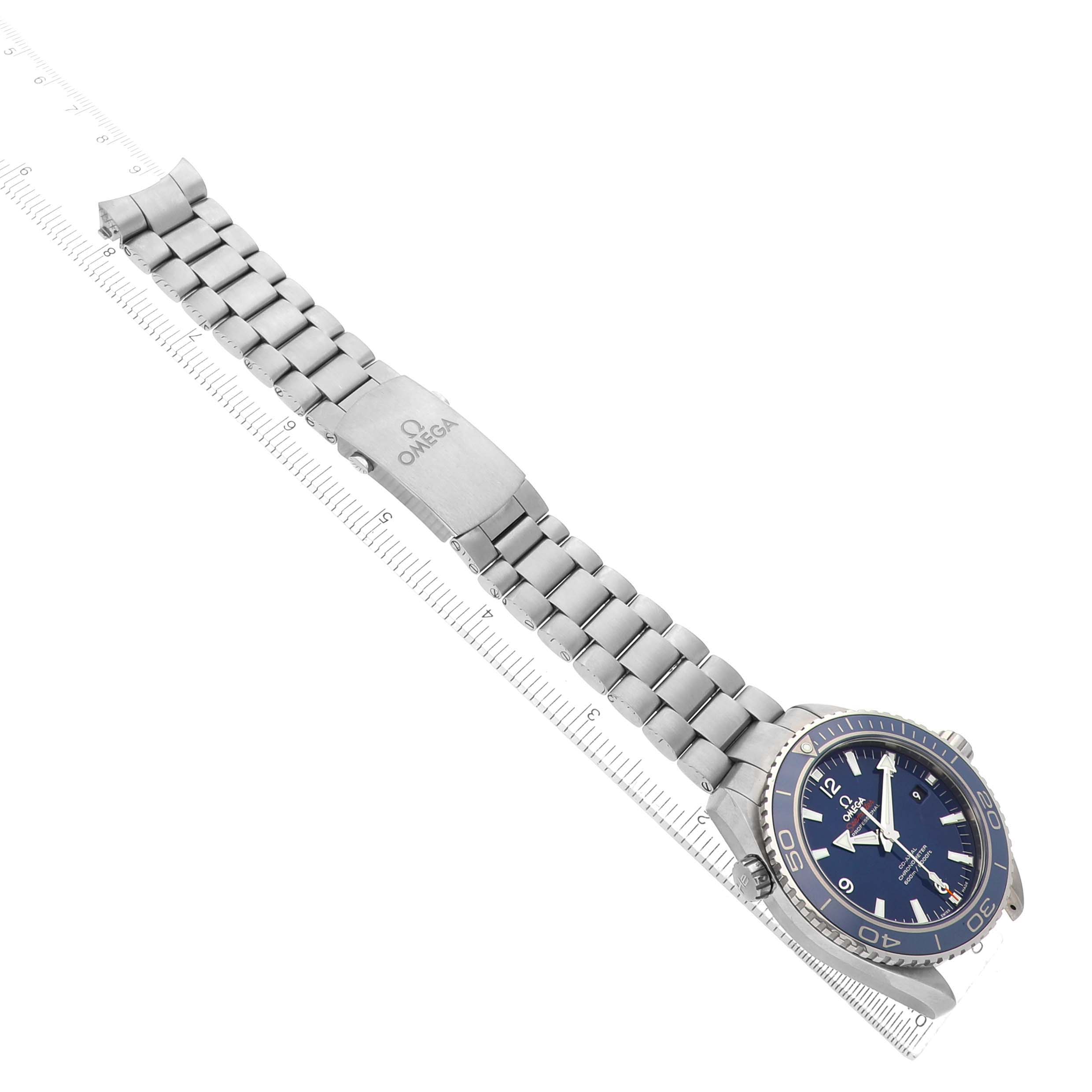 The Omega Seamaster 232.90.46.21.03.001 Men's Titanium Blue Dial watch is shown at an angle, with its face, bezel, and bracelet visible, including the clasp on a ruler.