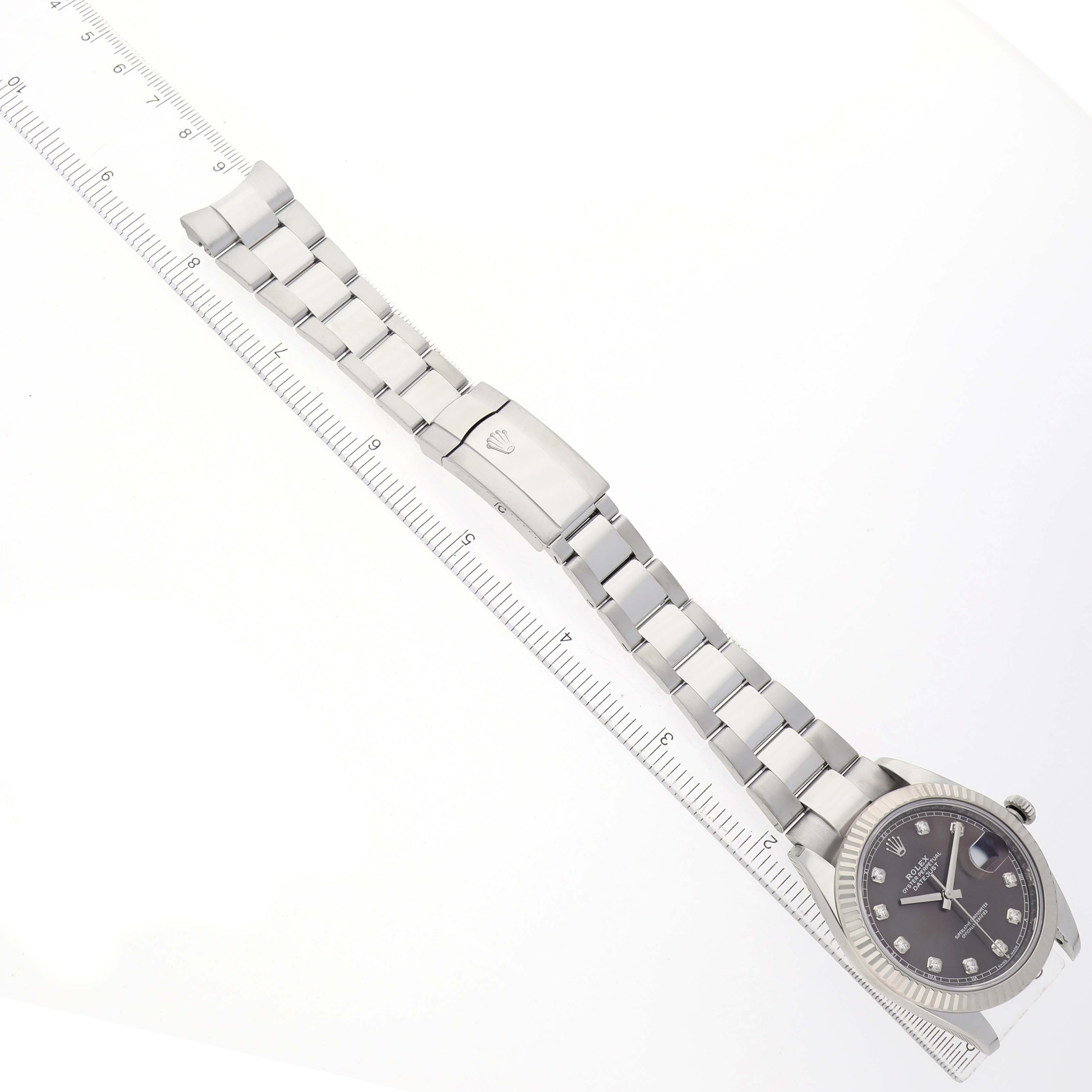 The image shows a top-down angle of a Rolex Datejust 41 126334 Men's Stainless Steel Grey Dial, highlighting the bracelet, clasp, and watch face alongside a ruler.