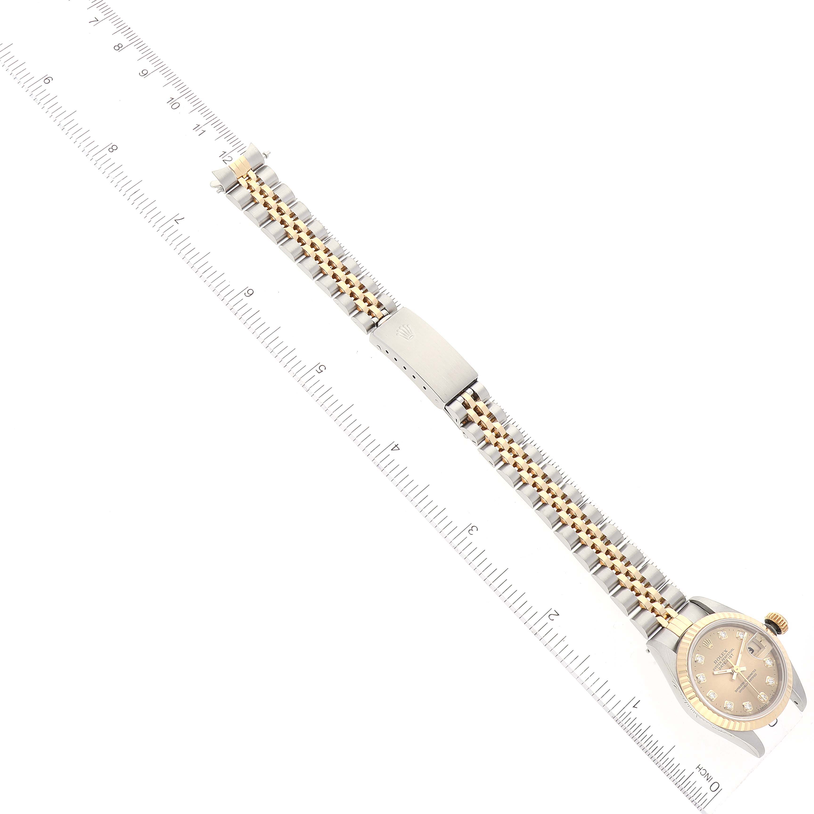 This is an overhead view of a Rolex Datejust 69173 Women's Steel and Gold (two tone) Champagne Dial 69173 Women's Steel and Gold (two tone) Champagne Dial watch showcasing the full band, clasp, and face placed along a measuring ruler.