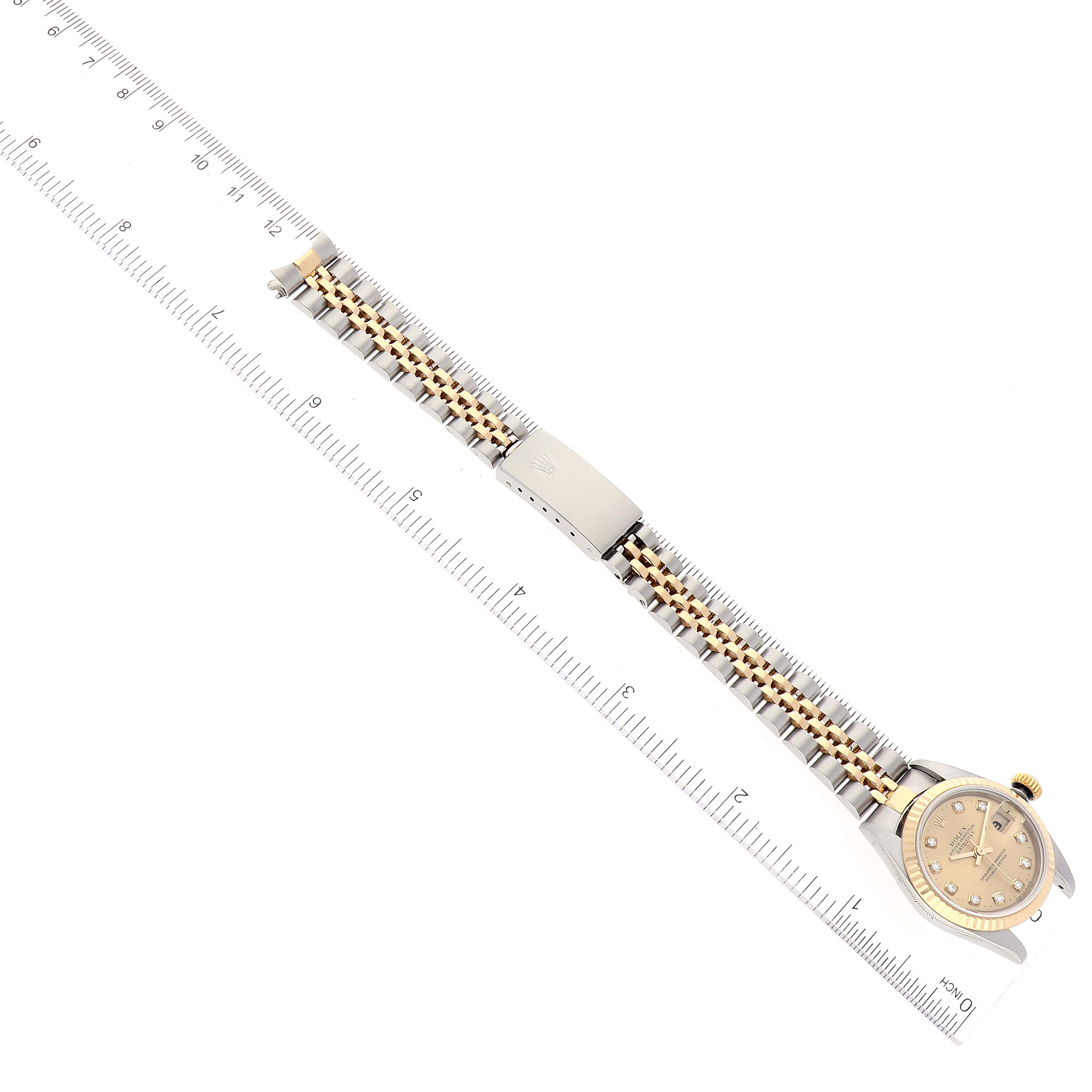 This image shows a Rolex Datejust 79173 Women's Steel and Gold (two tone) Champagne Dial 79173 Women's Steel and Gold (two tone) Champagne Dial watch lying flat, with the watchband fully extended and a ruler for scale.