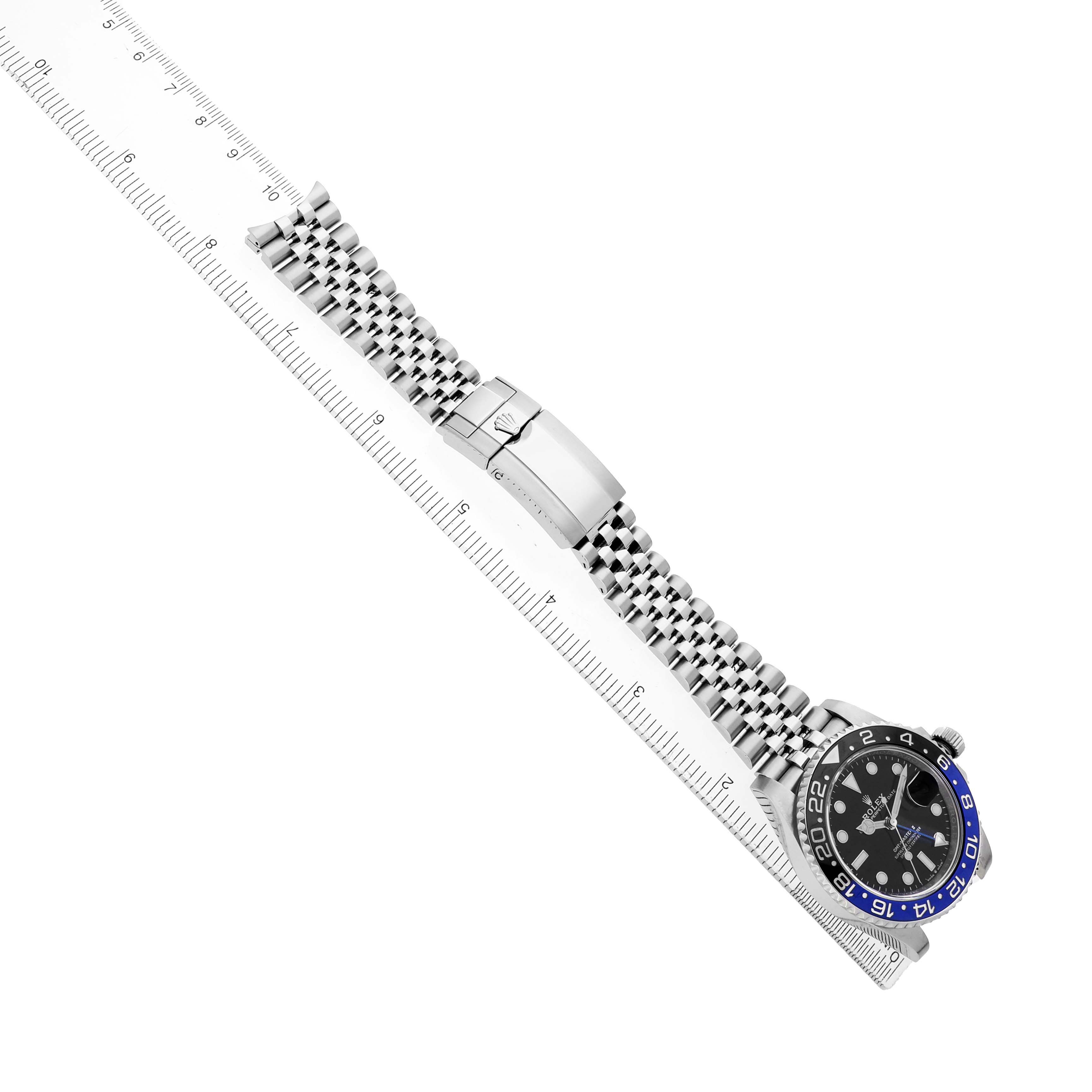 The Rolex GMT-Master 126710BLNR Men's Stainless Steel Black Dial watch is shown from a top view, highlighting the bracelet and clasp next to a ruler for scale.
