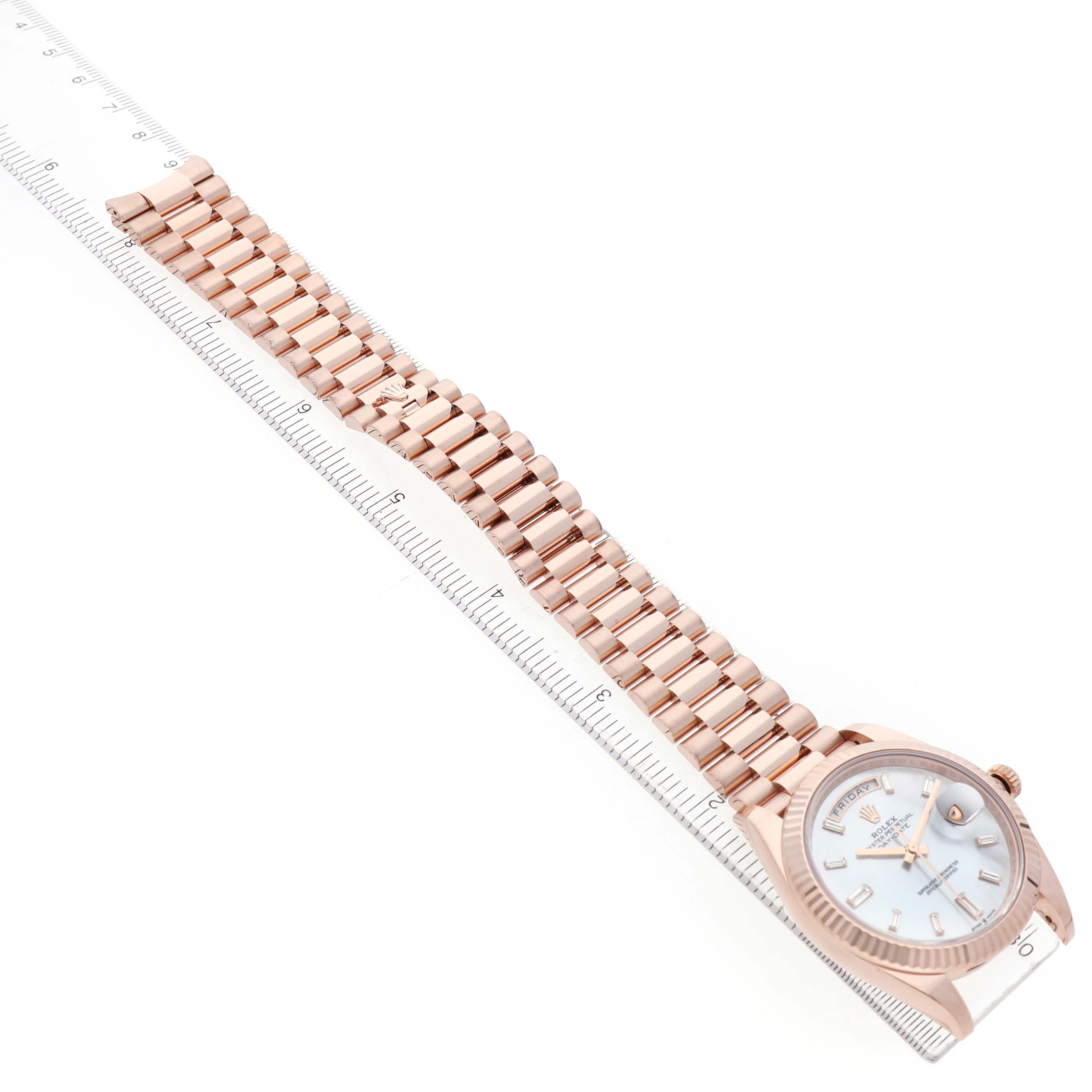 The Rolex President 228235 Men's Rose Gold Mother of Pearl Dial model watch is shown from an angled top view, highlighting the full bracelet and face alongside a ruler.