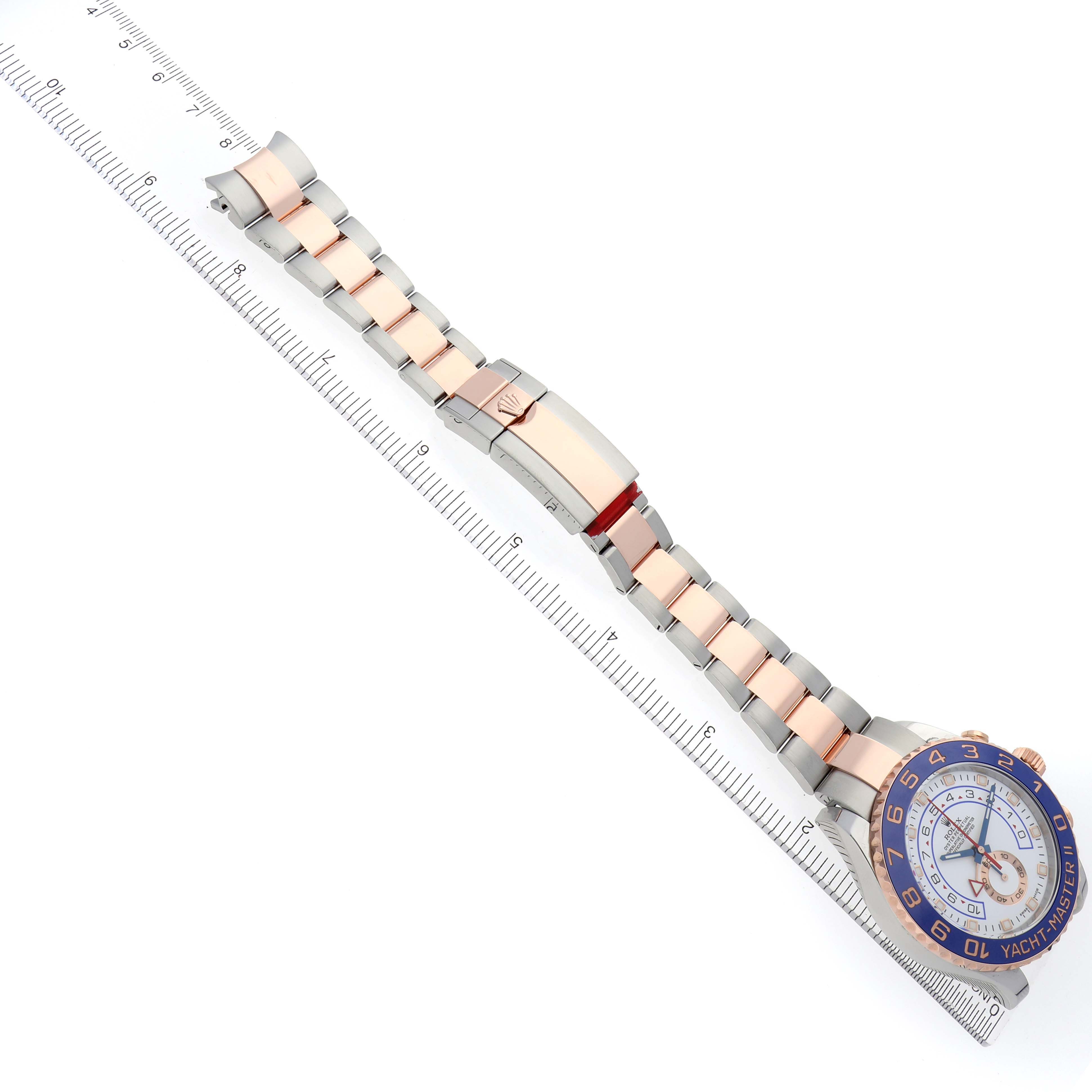 The Rolex Yacht-Master 116681 Men's Steel and Gold (two tone) White Dial 116681 Men's Steel and Gold (two tone) White Dial watch is shown diagonally, featuring the bracelet, clasp, and face alongside a ruler for scale.