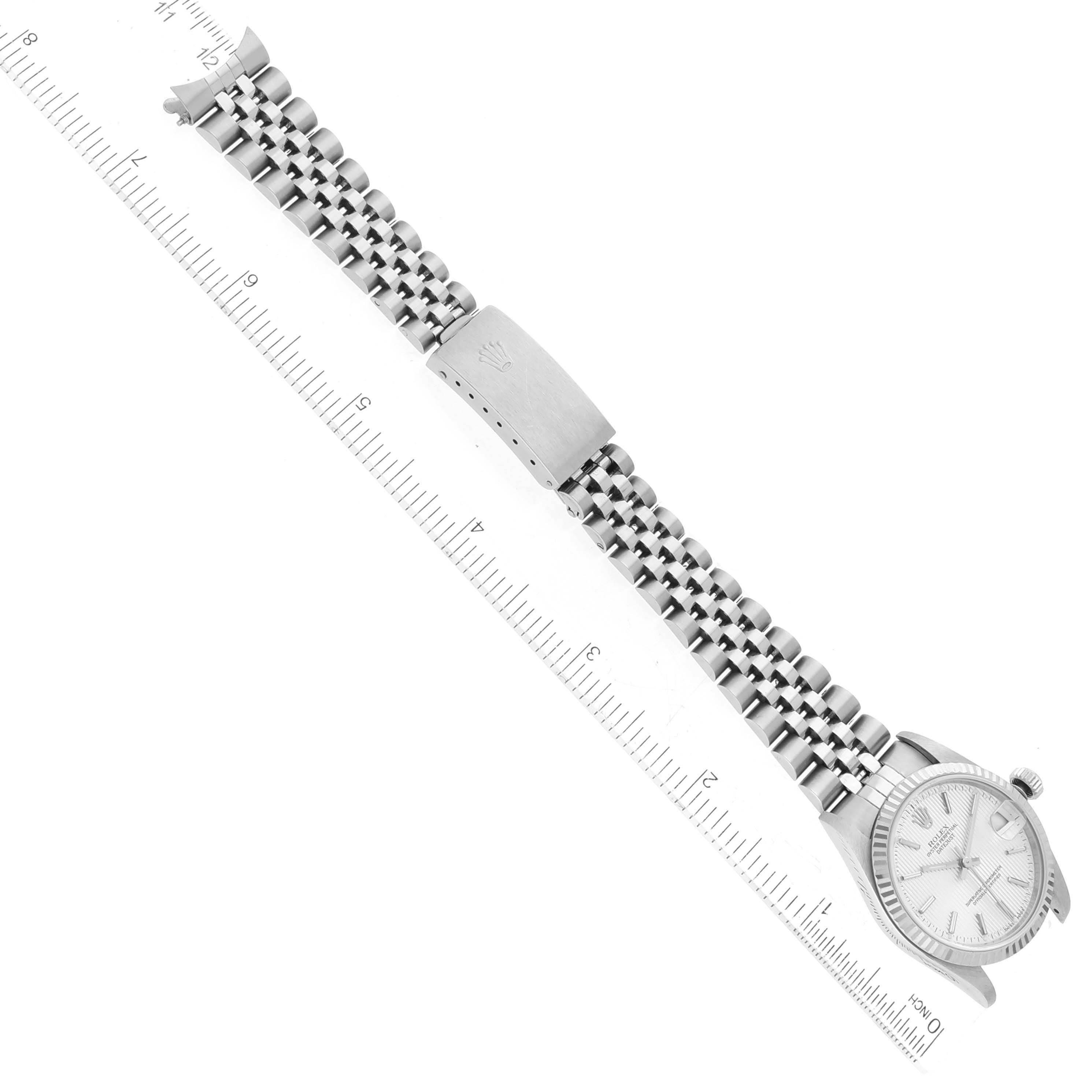 The Rolex Mid-Size 78274 Women's Stainless Steel Silver Dial 78274 Women's Stainless Steel Silver Dial model watch is shown from a top-down angle, featuring its face, bezel, and fully extended metal bracelet alongside a ruler.