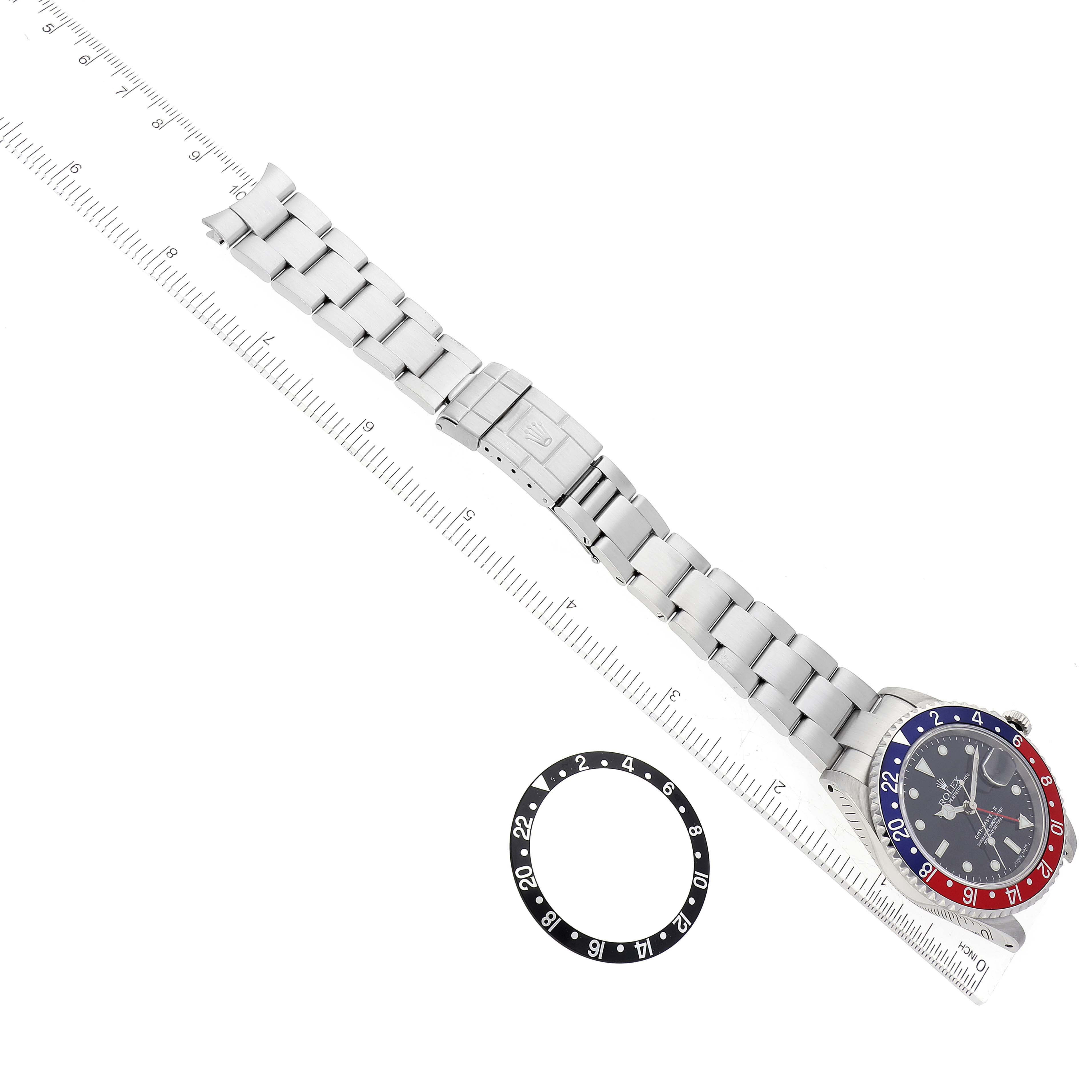 The image shows a Rolex GMT-Master 16710 Men
s Stainless Steel Black Dial 16710 Men
s Stainless Steel Black Dial watch laid flat with part of its bracelet, next to a separate black and white bezel insert, viewed from above.