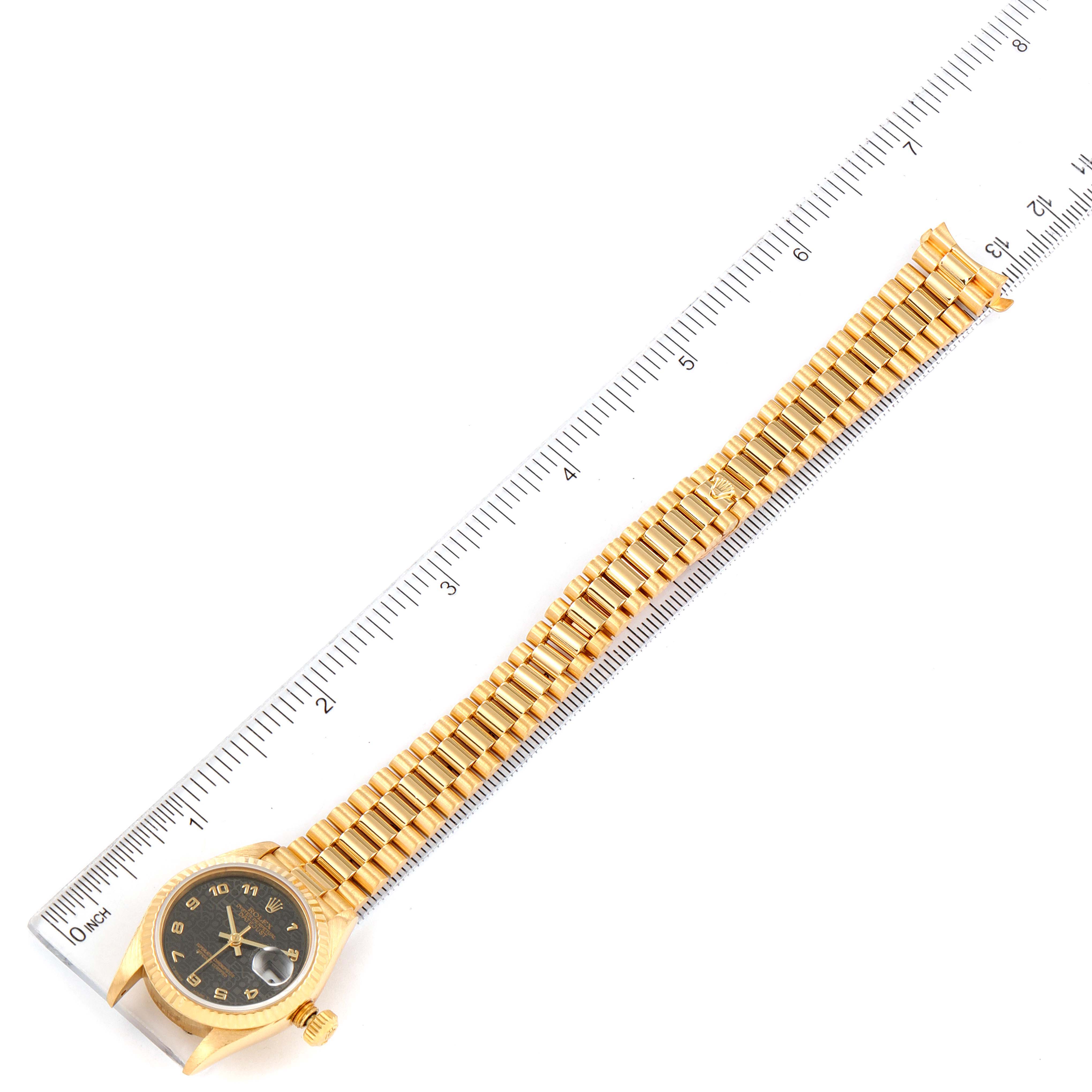 The image shows a top view of a Rolex President 69178 Women's Yellow Gold Black Dial 69178 Women's Yellow Gold Black Dial model watch laid alongside a ruler, displaying its face, bracelet, and crown.