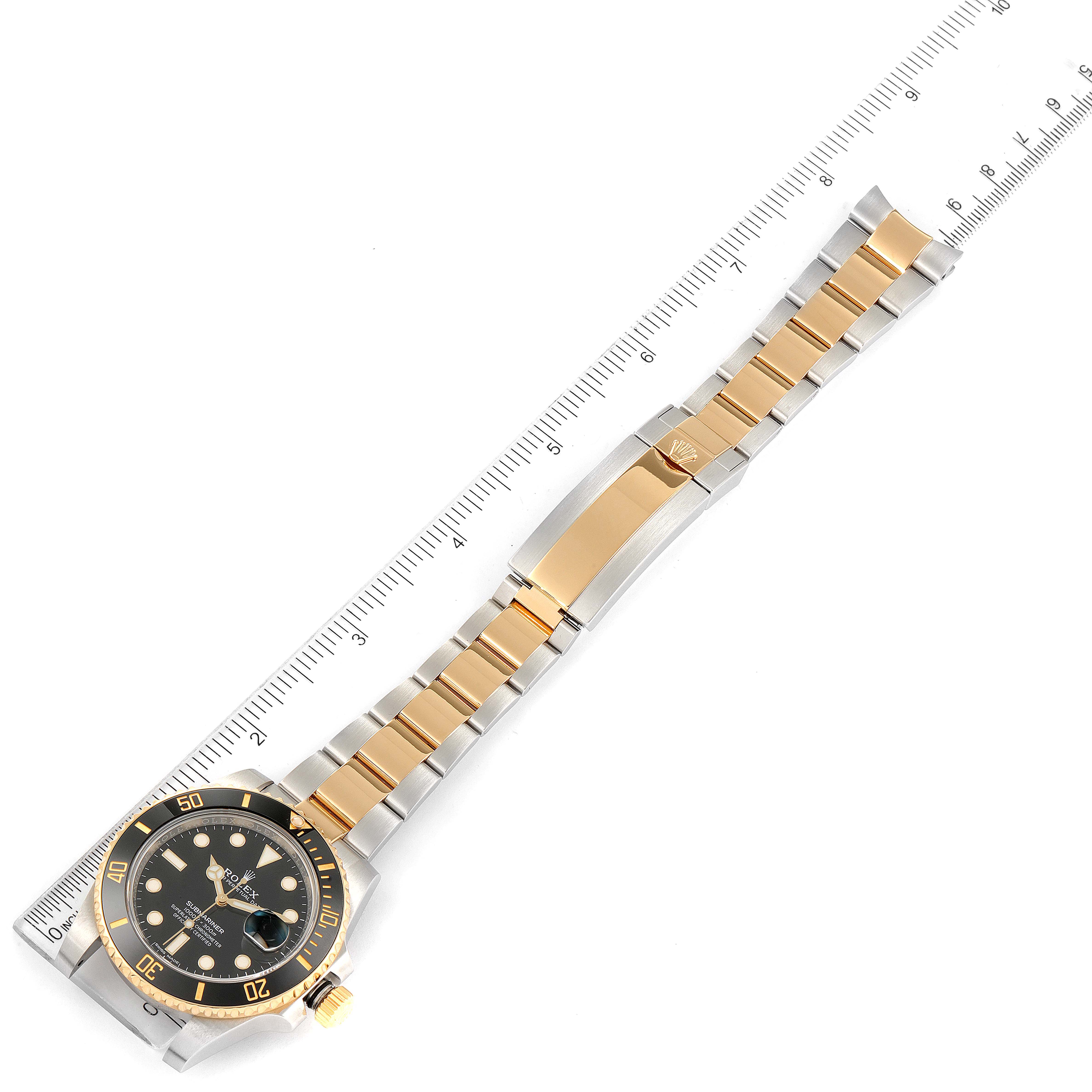 The image shows a top-down view of a Rolex Submariner 116613 Men's Steel and Gold (two tone) Black Dial 116613 Men's Steel and Gold (two tone) Black Dial watch with a gold and silver bracelet, next to a measuring ruler.