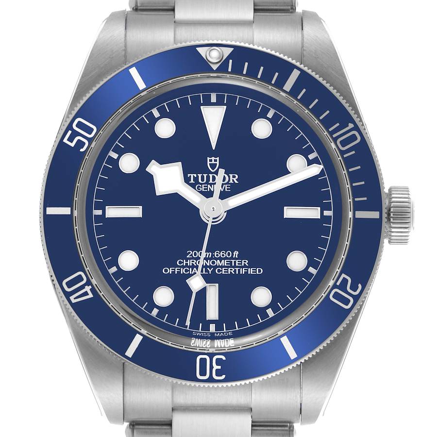 The Tudor Heritage Black Bay watch is shown from a frontal angle, highlighting its blue bezel, dial, and stainless steel bracelet.