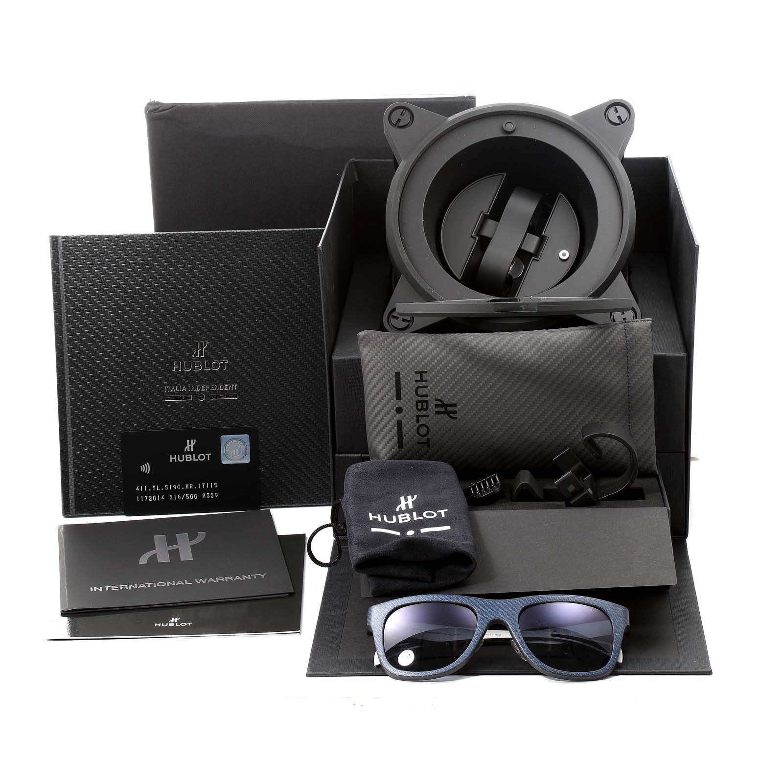 The image shows the Hublot Big Bang Unico 411.YL.5190.NR.ITI16 Men's Titanium Transparent Dial 411.YL.5190.NR.ITI16 Men's Titanium Transparent Dial packaging, including warranty, case, sunglasses, and various accessories from a top-angle view.