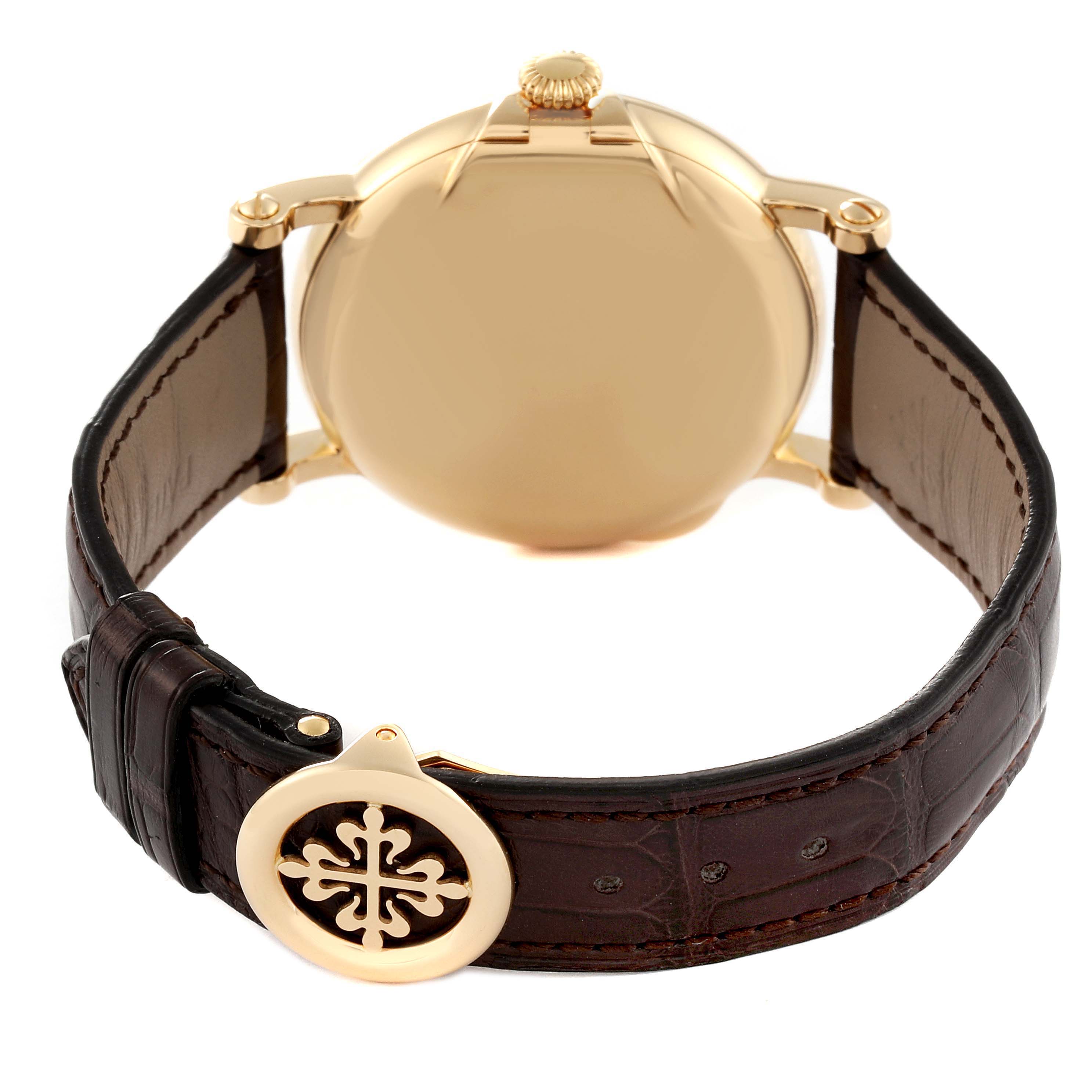 The image shows the back of the Patek Philippe Calatrava 5153J-001 Men's Yellow Gold Silver Dial watch with a focus on its gold case and brown leather strap with a decorative clasp.