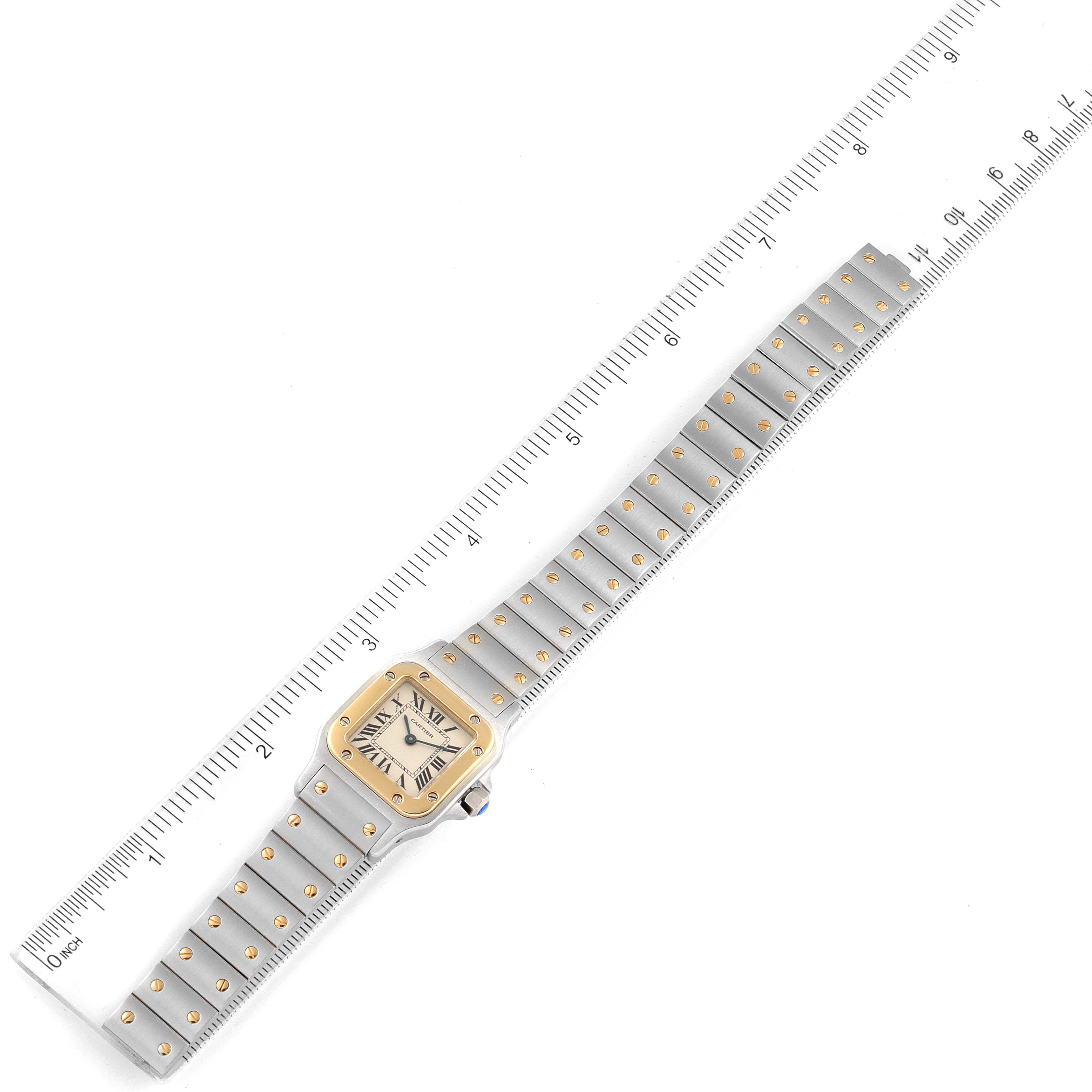 The Cartier Santos W20012C4 Women's Steel and Gold (two tone) Silver Dial W20012C4 Women's Steel and Gold (two tone) Silver Dial watch is shown from a top-down angle, displaying the face and full metal strap against a ruler for scale.