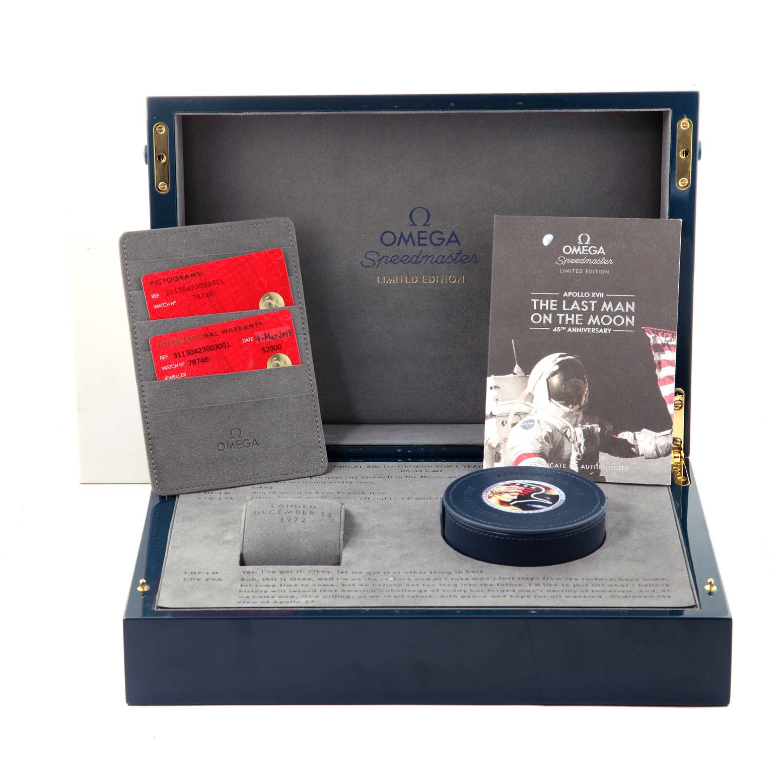 The image shows an opened Omega Speedmaster 311.30.42.30.03.001 Men's Stainless Steel Blue Dial 311.30.42.30.03.001 Men's Stainless Steel Blue Dial watch box with certification cards, a booklet, and a circular tin.