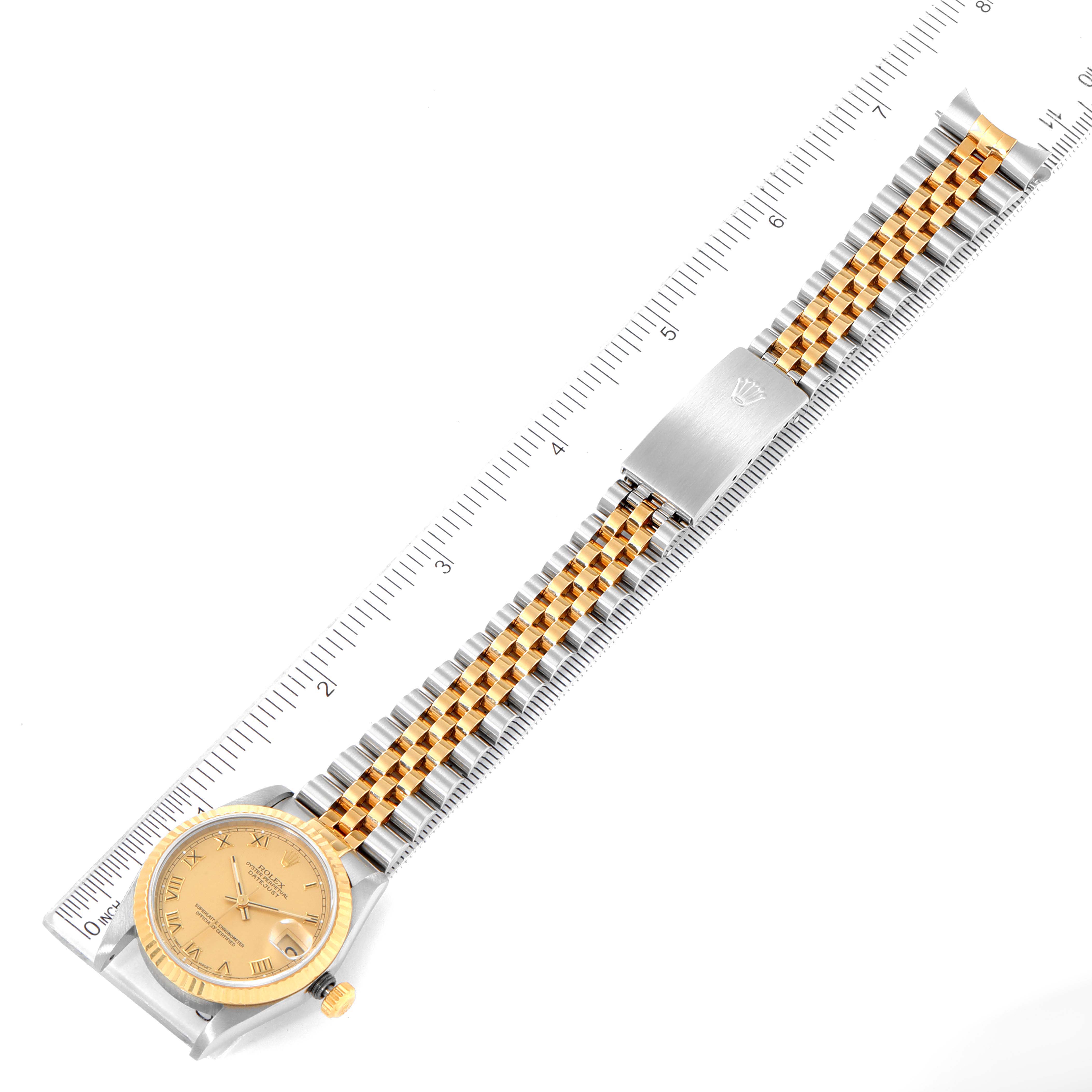 The Rolex Mid-Size 68273 Women
s Steel and Gold (two tone) Champagne Dial 68273 Women
s Steel and Gold (two tone) Champagne Dial model watch is shown from an overhead angle, displaying its face, bracelet, and clasp placed beside a ruler.