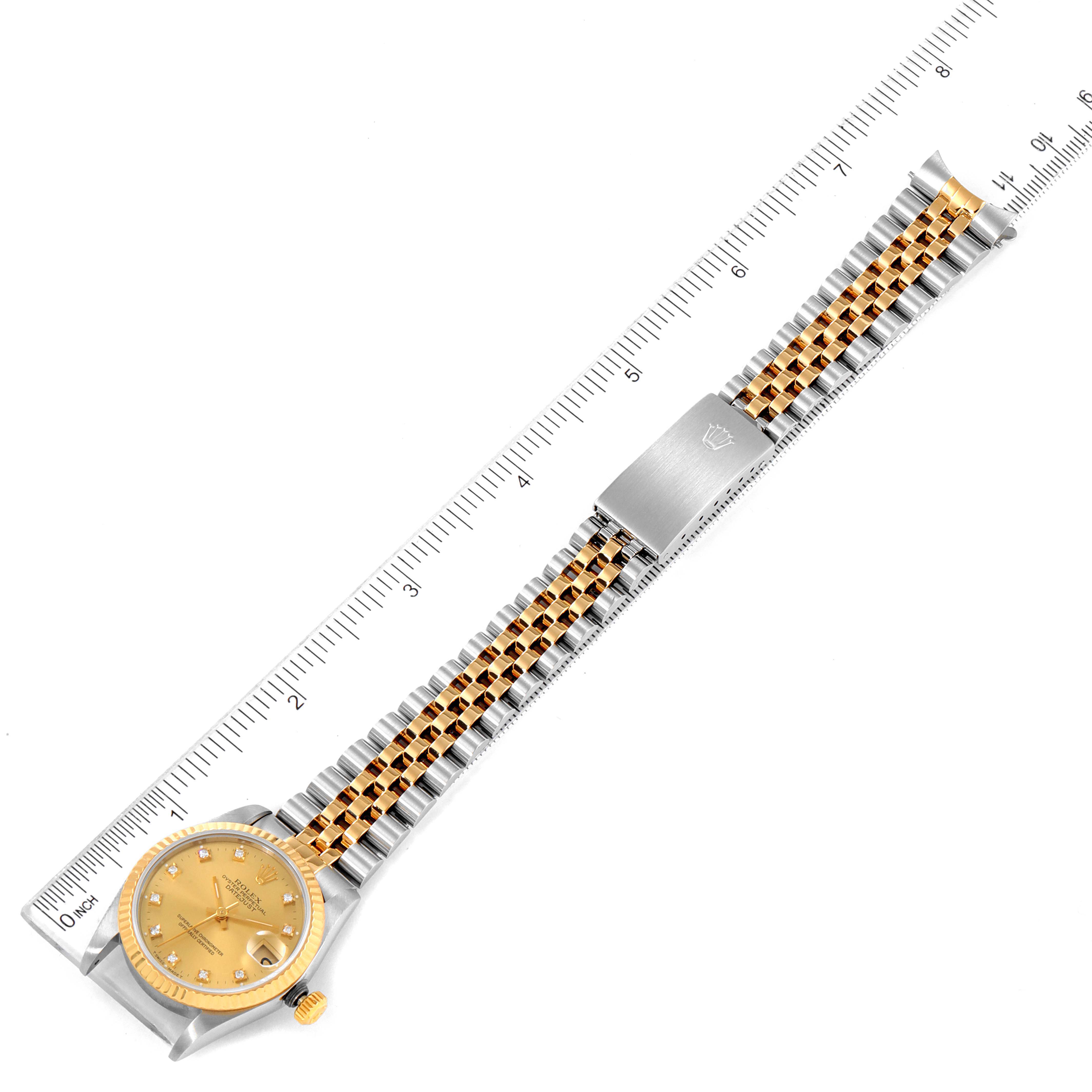 The image shows a top-down view of a Rolex Mid-Size 68273 Women
s Steel and Gold (two tone) Champagne Dial 68273 Women
s Steel and Gold (two tone) Champagne Dial watch with a gold dial and a two-tone bracelet placed alongside a ruler.