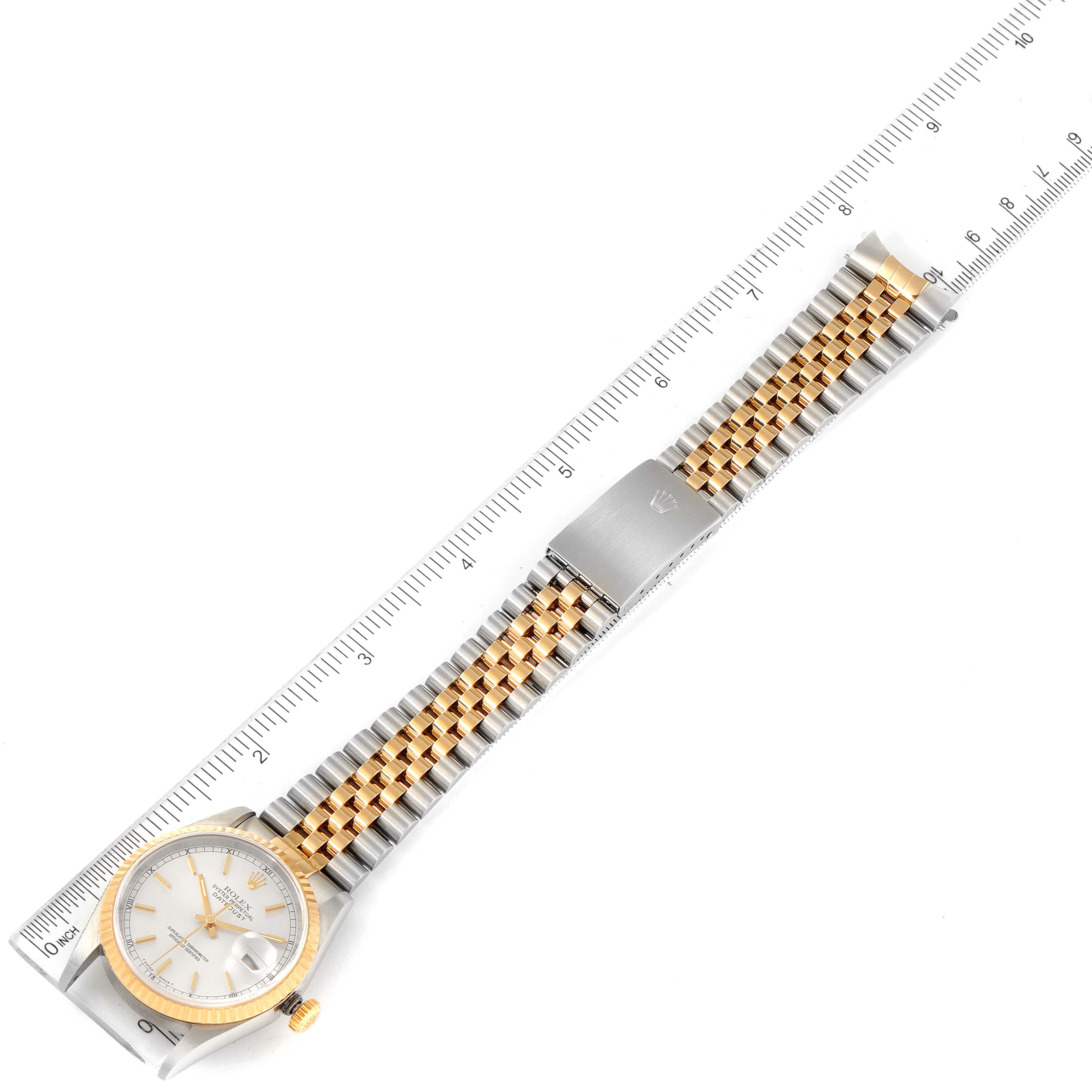 The Rolex Datejust 16233 Men's Steel and Gold (two tone) Silver Dial 16233 Men's Steel and Gold (two tone) Silver Dial watch is shown from a top-down angle, displaying the full face, bracelet, and clasp with a ruler for scale.