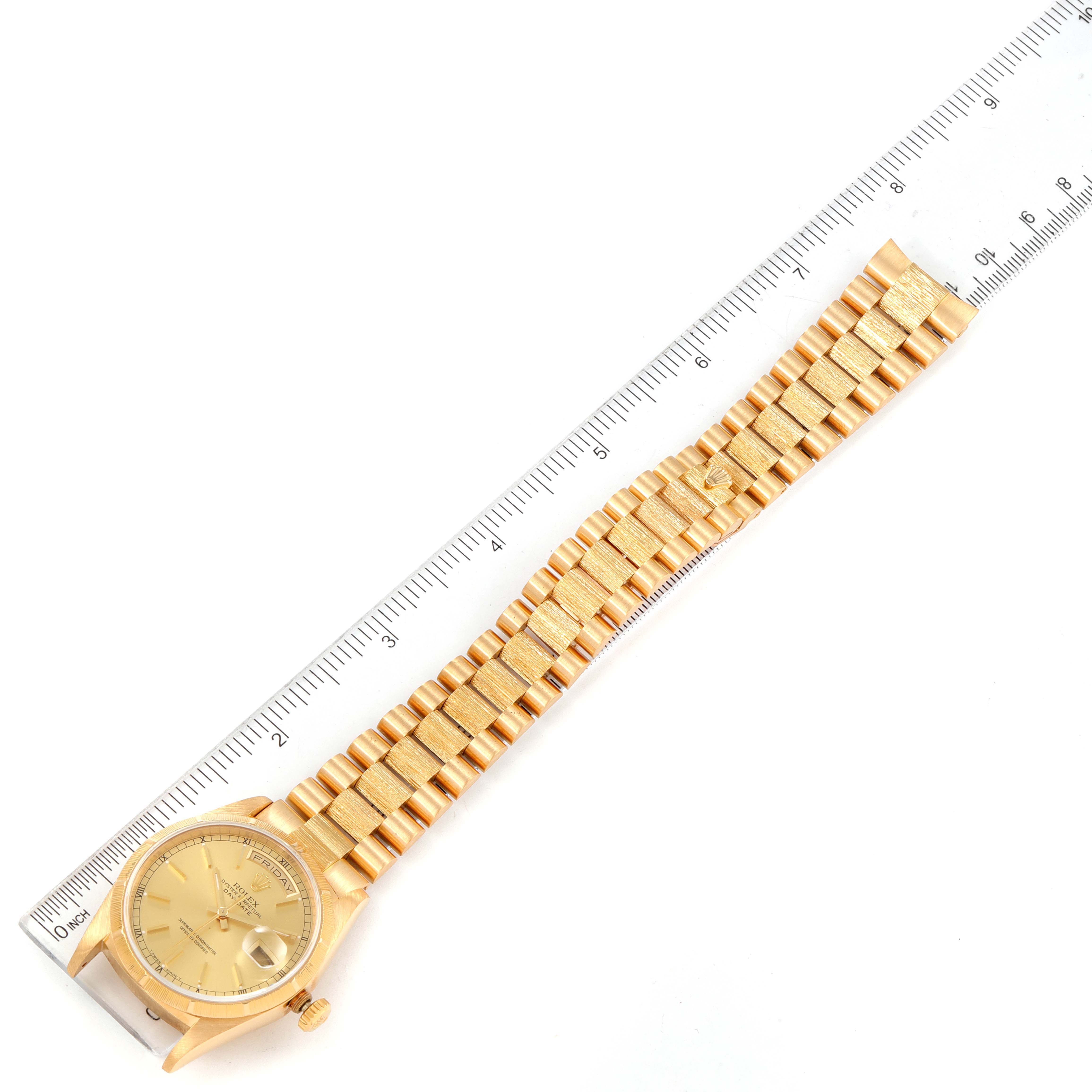 This top-down view of the Rolex President 18248 Men's Yellow Gold Champagne Dial 18248 Men's Yellow Gold Champagne Dial model watch showcases its face and entire gold bracelet next to a ruler for scale.