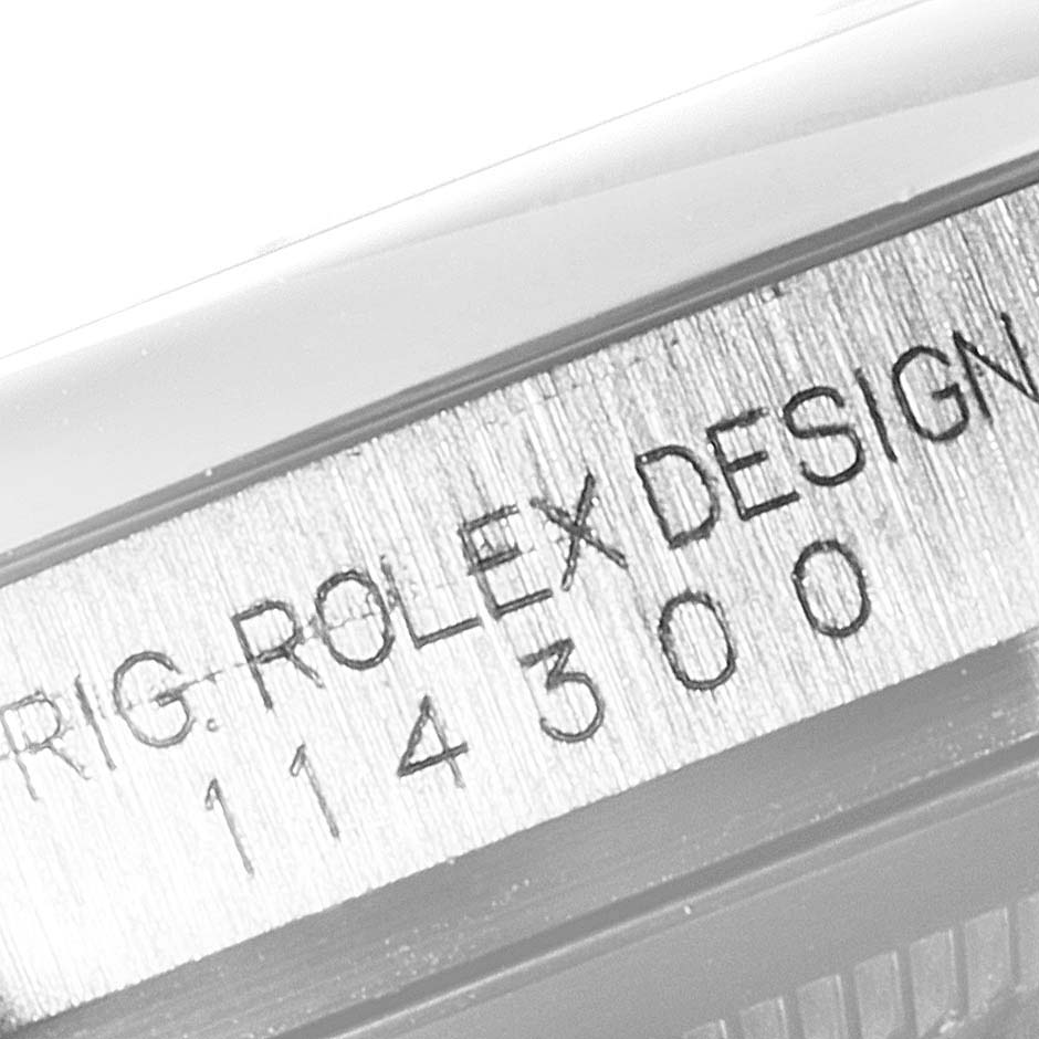 The image shows a close-up of the serial number engraving on the side of the Rolex Oyster Perpetual 114300 Men's Stainless Steel Grey Dial 114300 Men's Stainless Steel Grey Dial watch case.
