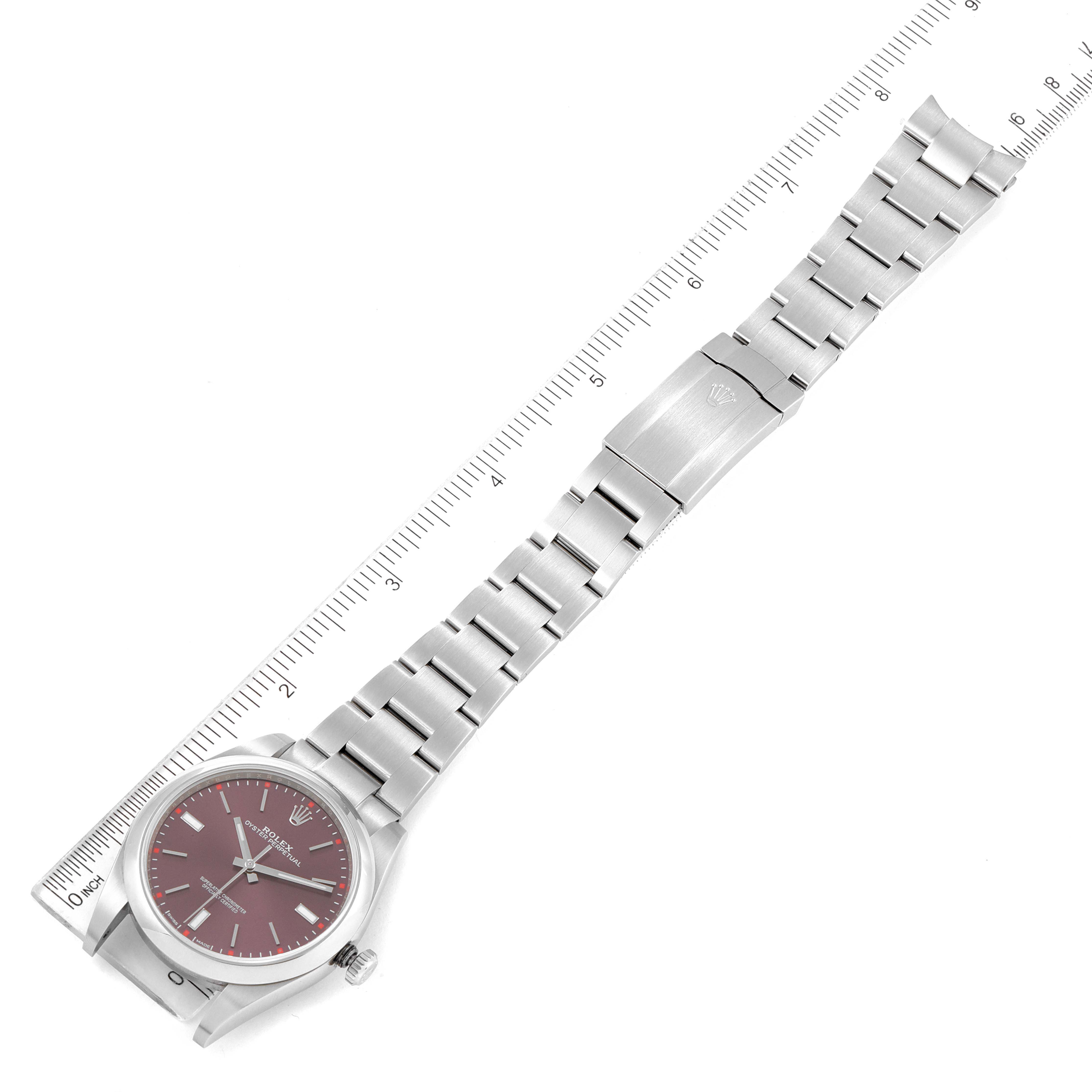 This image shows a top-down view of a Rolex Oyster Perpetual 114300 Men
s Stainless Steel Burgundy Dial 114300 Men
s Stainless Steel Burgundy Dial watch with a ruler alongside, displaying the bracelet and face.