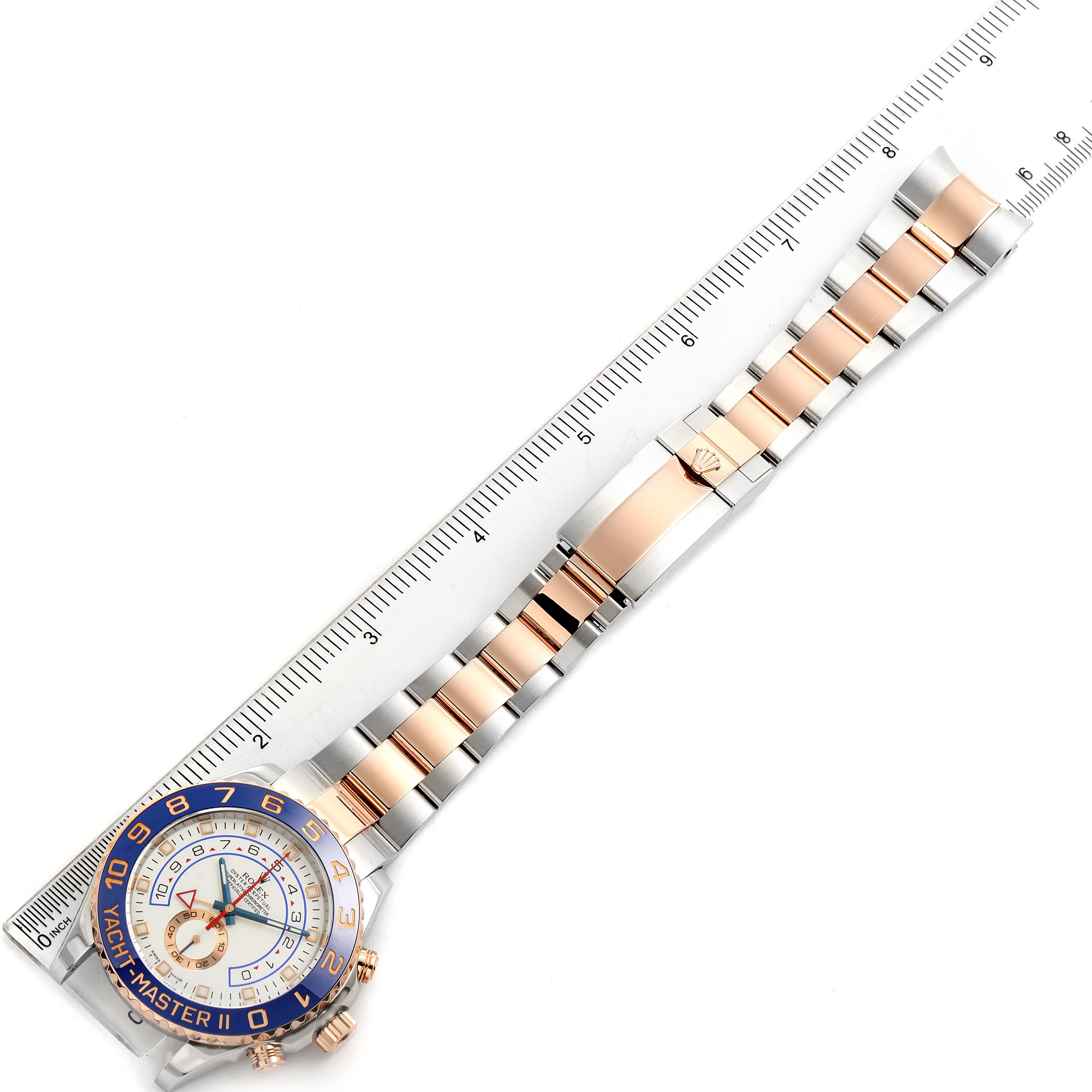 The image shows a top view of a Rolex Yacht-Master 116681 Men's Rose Gold White Dial 116681 Men's Rose Gold White Dial watch resting along a ruler, displaying the face, bezel, and bracelet.