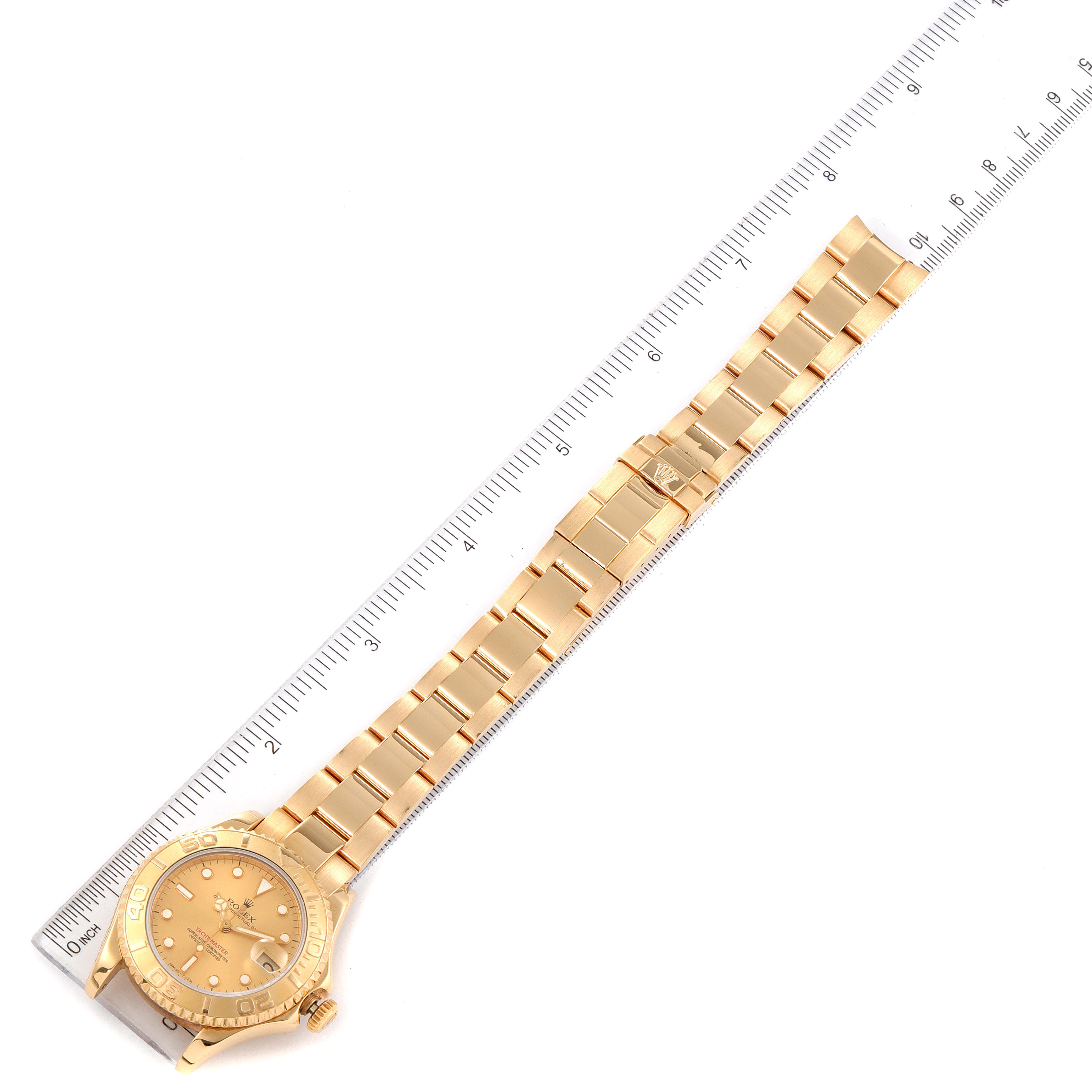 The image shows a Rolex Yacht-Master 68628 Men's Yellow Gold Champagne Dial 68628 Men's Yellow Gold Champagne Dial watch laid flat next to a ruler, displaying the watch face and full metal band.