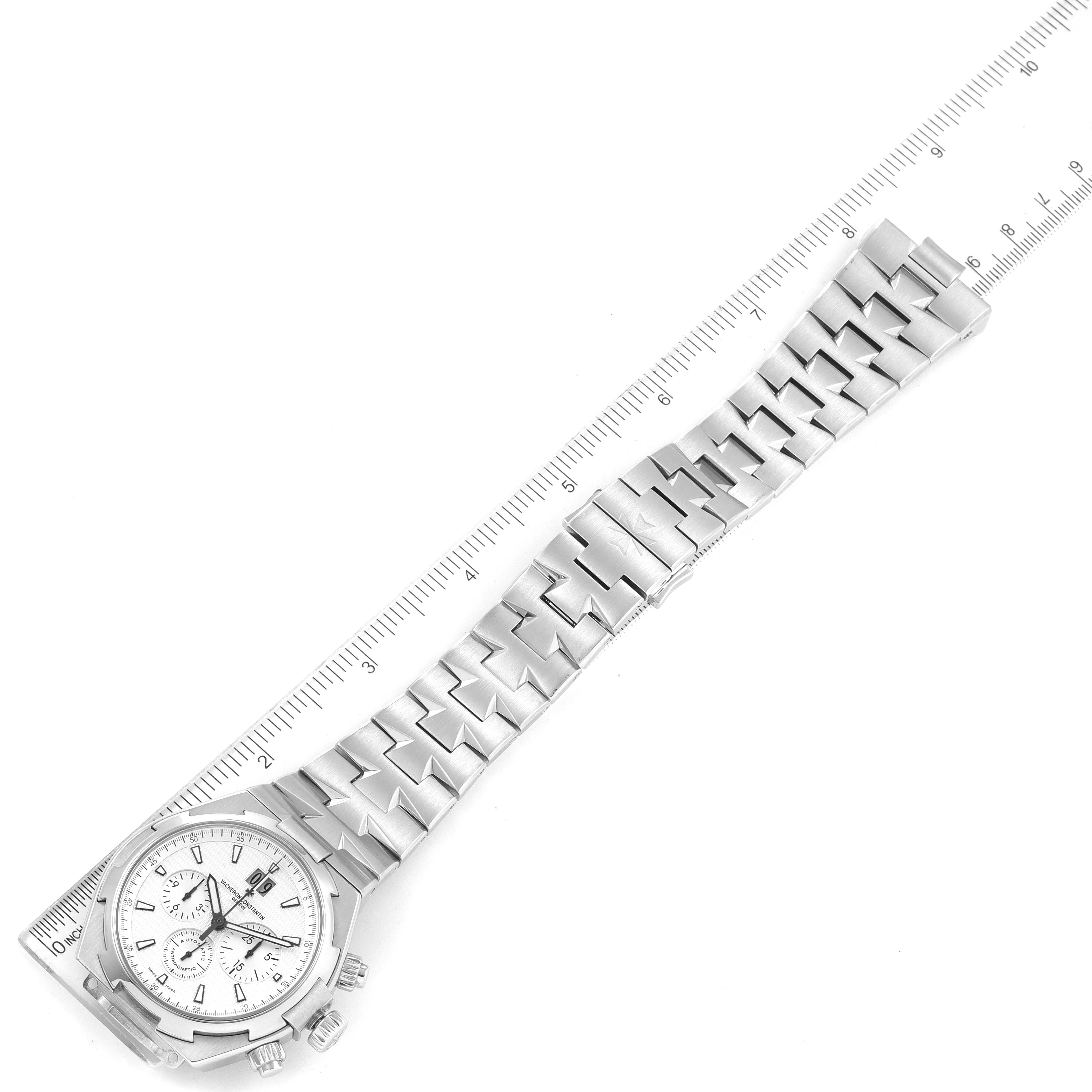 The image shows the Vacheron Constantin Overseas 49150/B01A-9095 Men's Stainless Steel Silver Dial 49150/B01A-9095 Men's Stainless Steel Silver Dial watch laid flat, highlighting the face and bracelet with a ruler for scale.