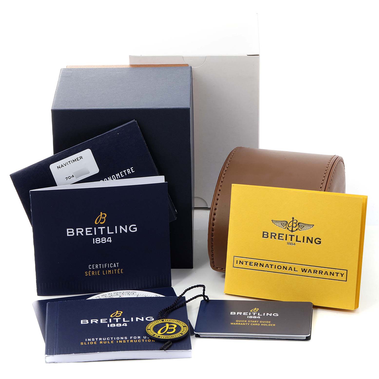 The image shows an assortment of accessories for a Navitimer model by Breitling, including manuals, warranty cards, packing materials, and a brown watch case.