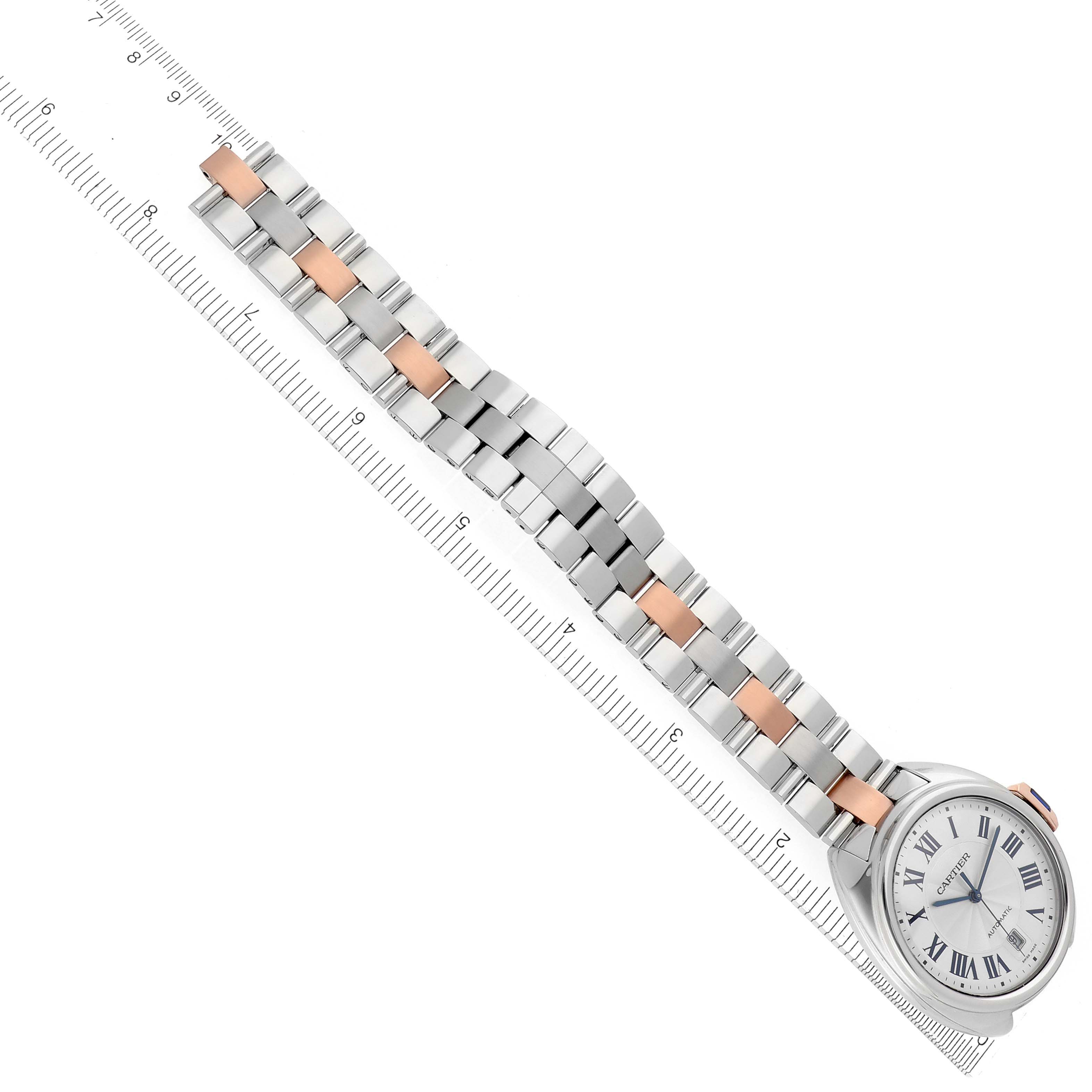 The Cartier Clé watch is shown at an overhead angle, displaying the full face and two-tone bracelet alongside a ruler.