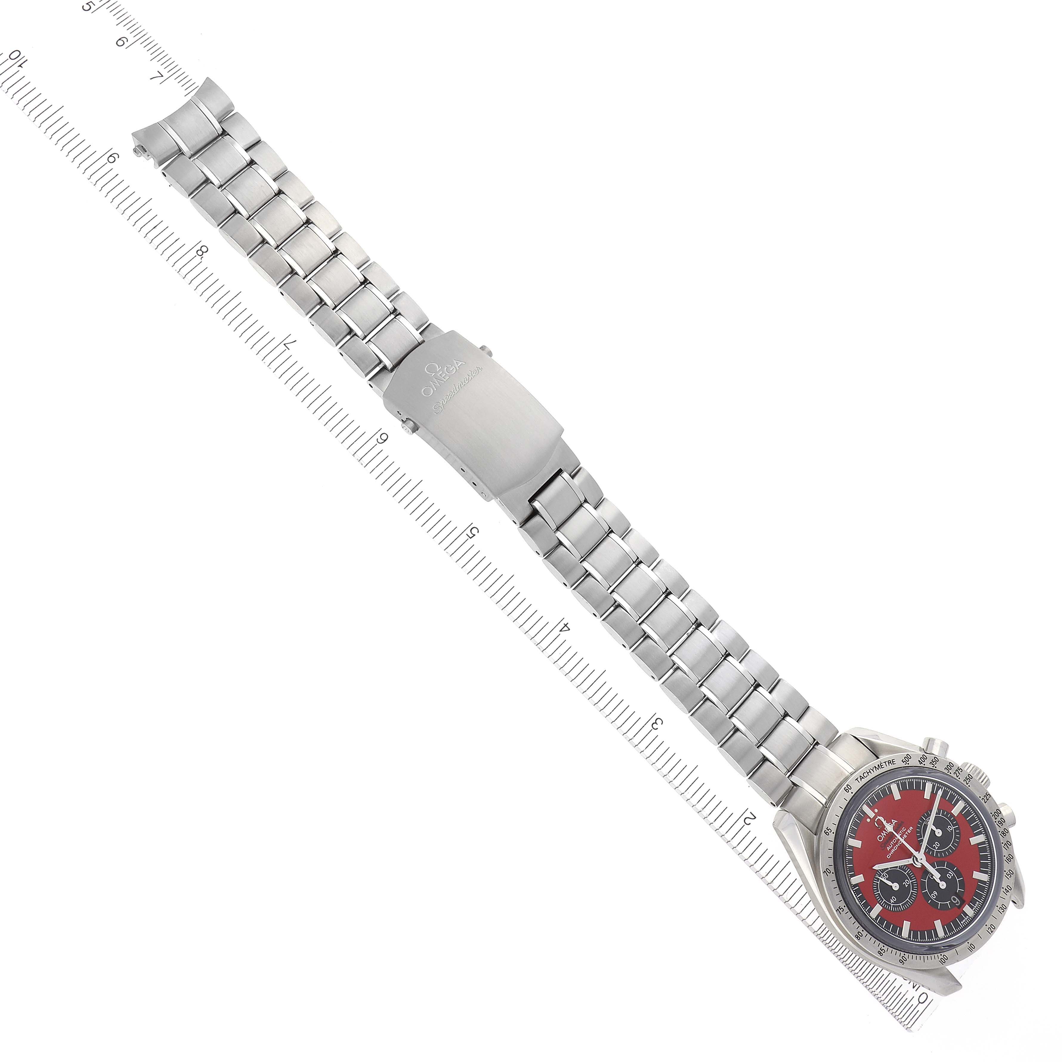 The Omega Speedmaster 3506.61.00 Men
s Stainless Steel Red Dial 3506.61.00 Men
s Stainless Steel Red Dial watch is shown from a top-down angle, featuring the full bracelet, clasp, and watch face next to a ruler.