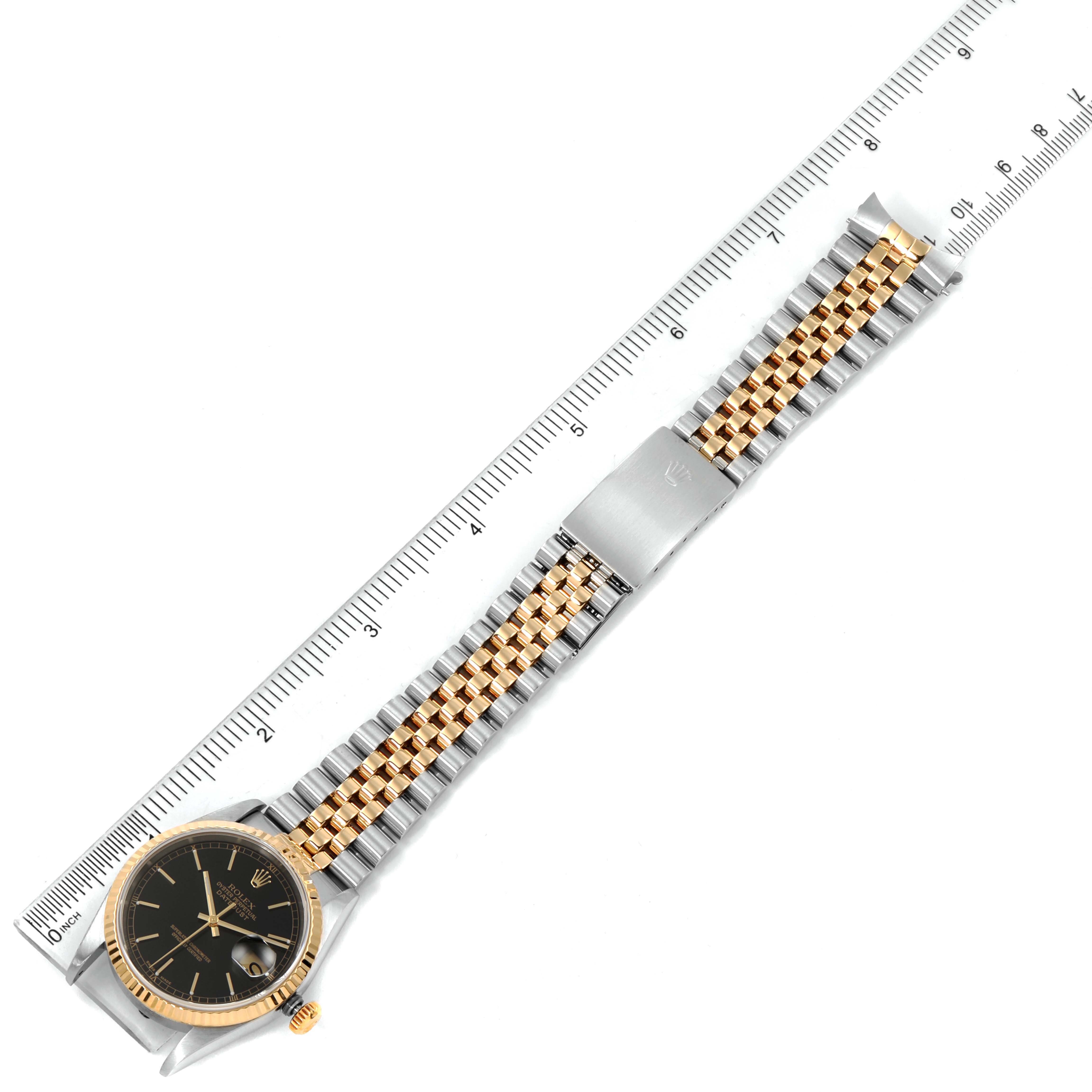 The image shows a top-down view of a Rolex Datejust 16233 Men's Steel and Gold (two tone) Black Dial 16233 Men's Steel and Gold (two tone) Black Dial watch, displaying the face, bracelet, and a clasp against a ruler.