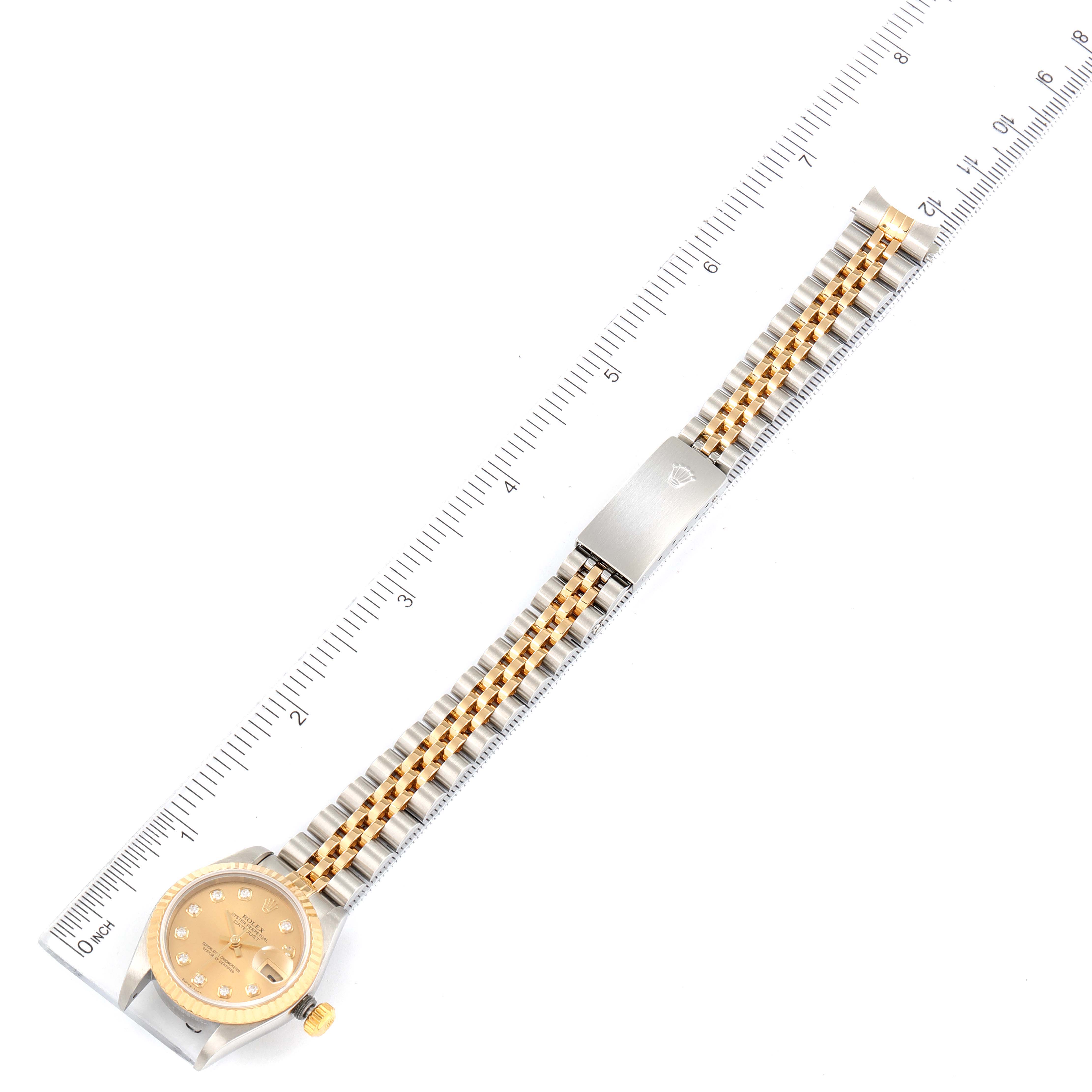 The image shows a top view of a Rolex Datejust 79173 Women
s Steel and Gold (two tone) Champagne Dial 79173 Women
s Steel and Gold (two tone) Champagne Dial watch with its bracelet extended and aligned with a ruler for measurement.