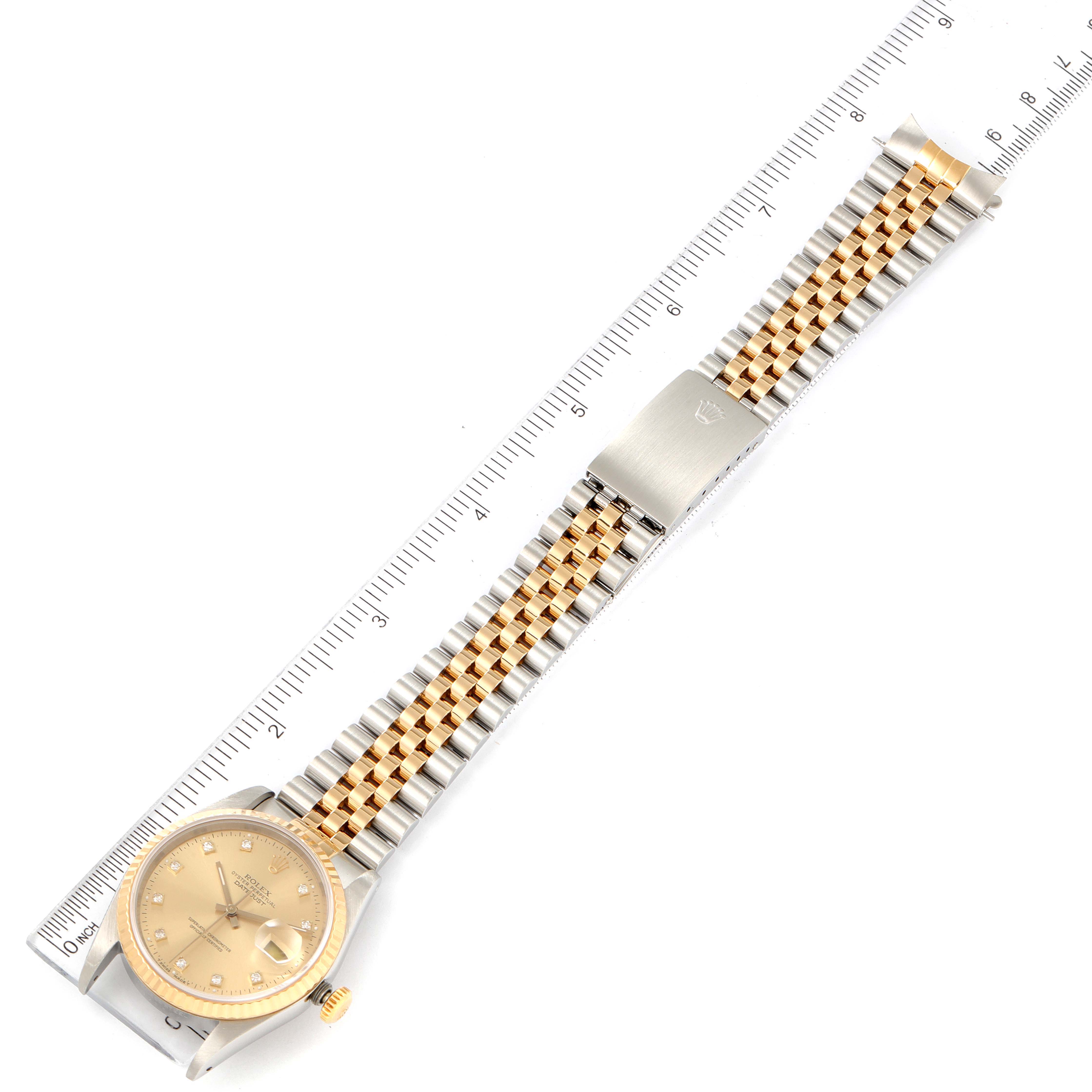 This is an aerial view of a Rolex Datejust 16233 Men's Steel and Gold (two tone) Champagne Dial 16233 Men's Steel and Gold (two tone) Champagne Dial watch, showing its face and two-tone bracelet next to a ruler for scale.