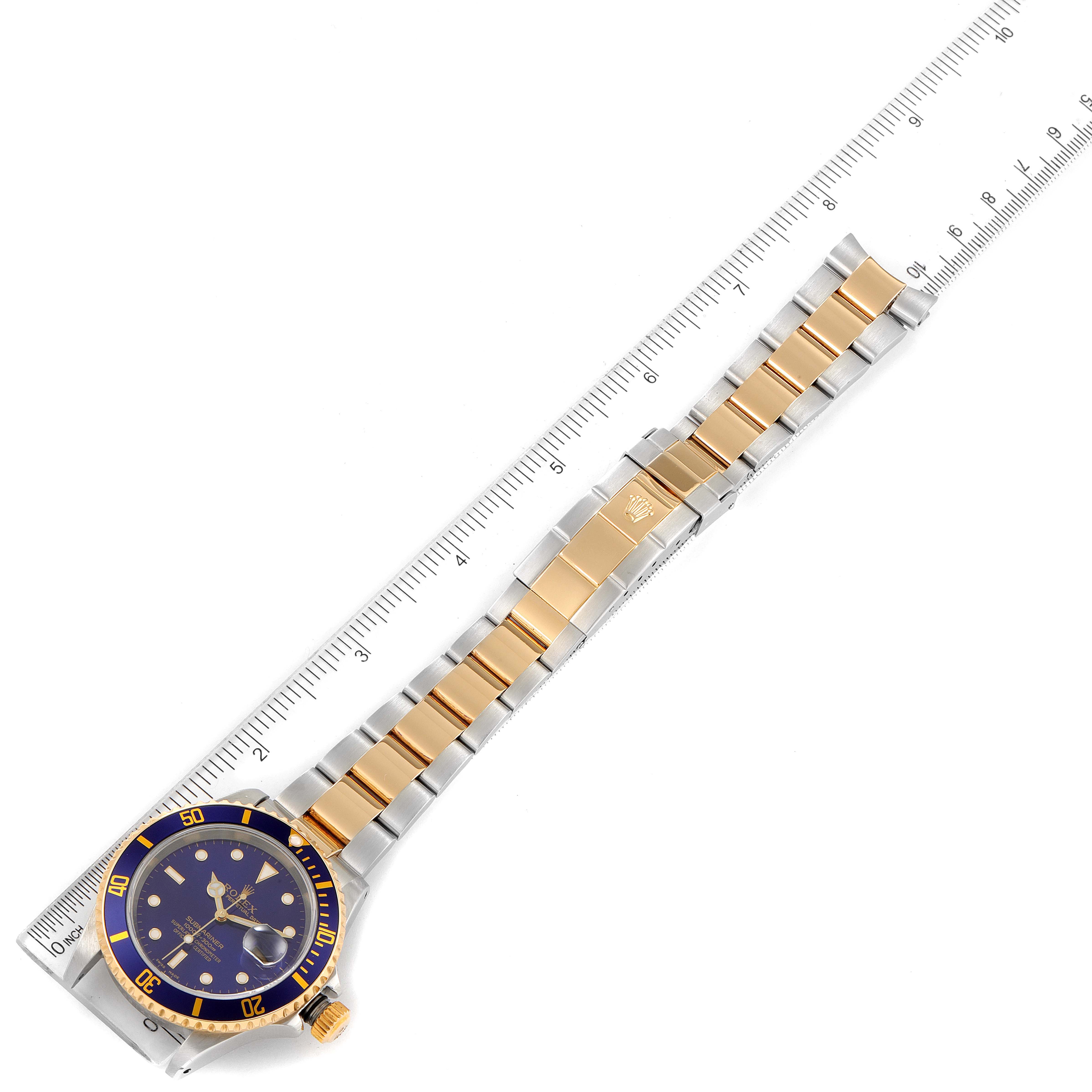 This image shows a Rolex Submariner 16613 Men
s Steel and Gold (two tone) Blue Dial 16613 Men
s Steel and Gold (two tone) Blue Dial watch laid flat with a ruler beside it, revealing the face, bezel, and bracelet.